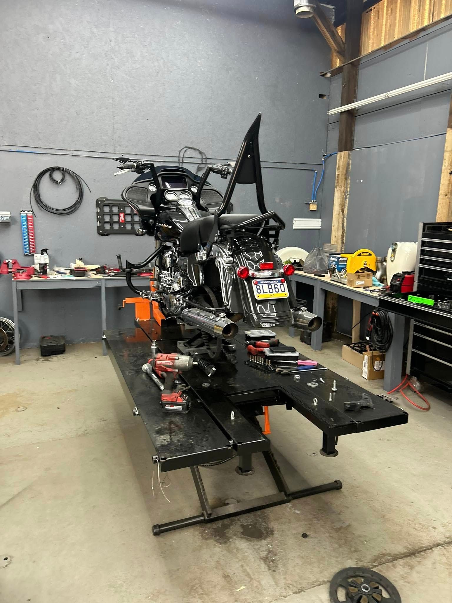 Motorcycle on a lift in a workshop, tools and equipment visible around the bike.