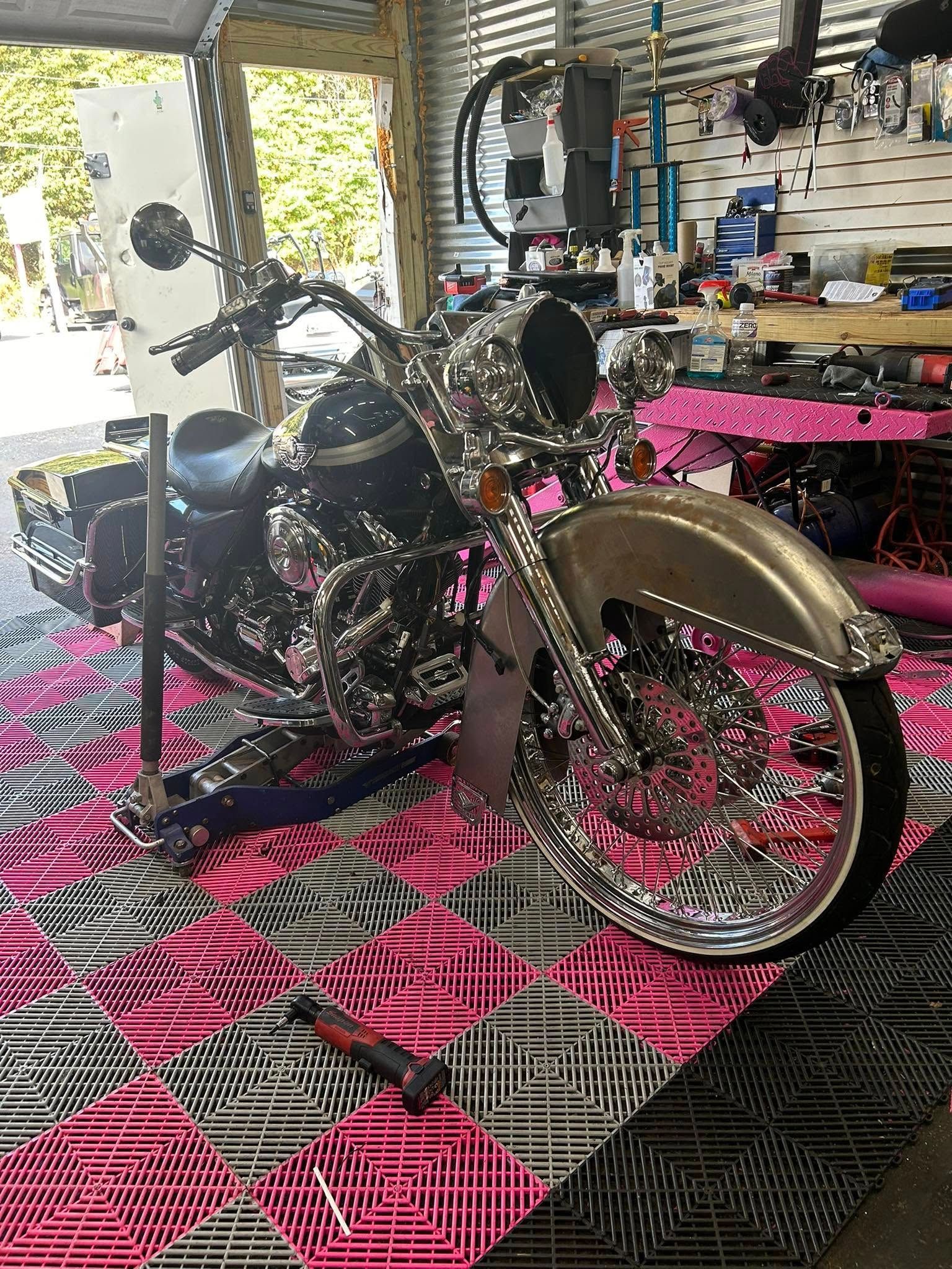 Shiny chrome motorcycle, pink and black patterned floor, tools in a workshop.