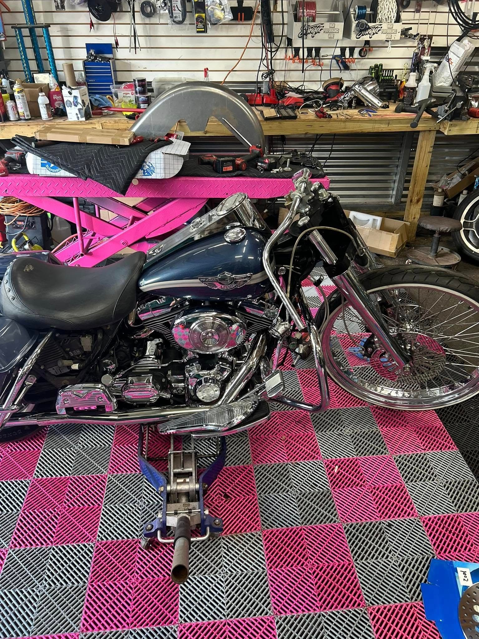 Motorcycle with chrome accents, black seat, and pink accents in a garage setting with pink and black checkered floor.