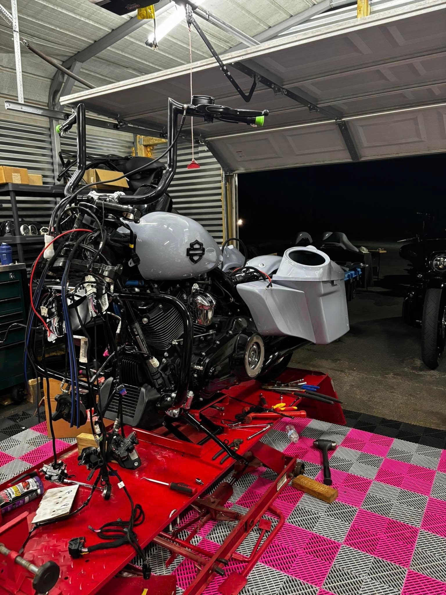 Motorcycle being worked on inside a garage; wires exposed, parts on a red lift.