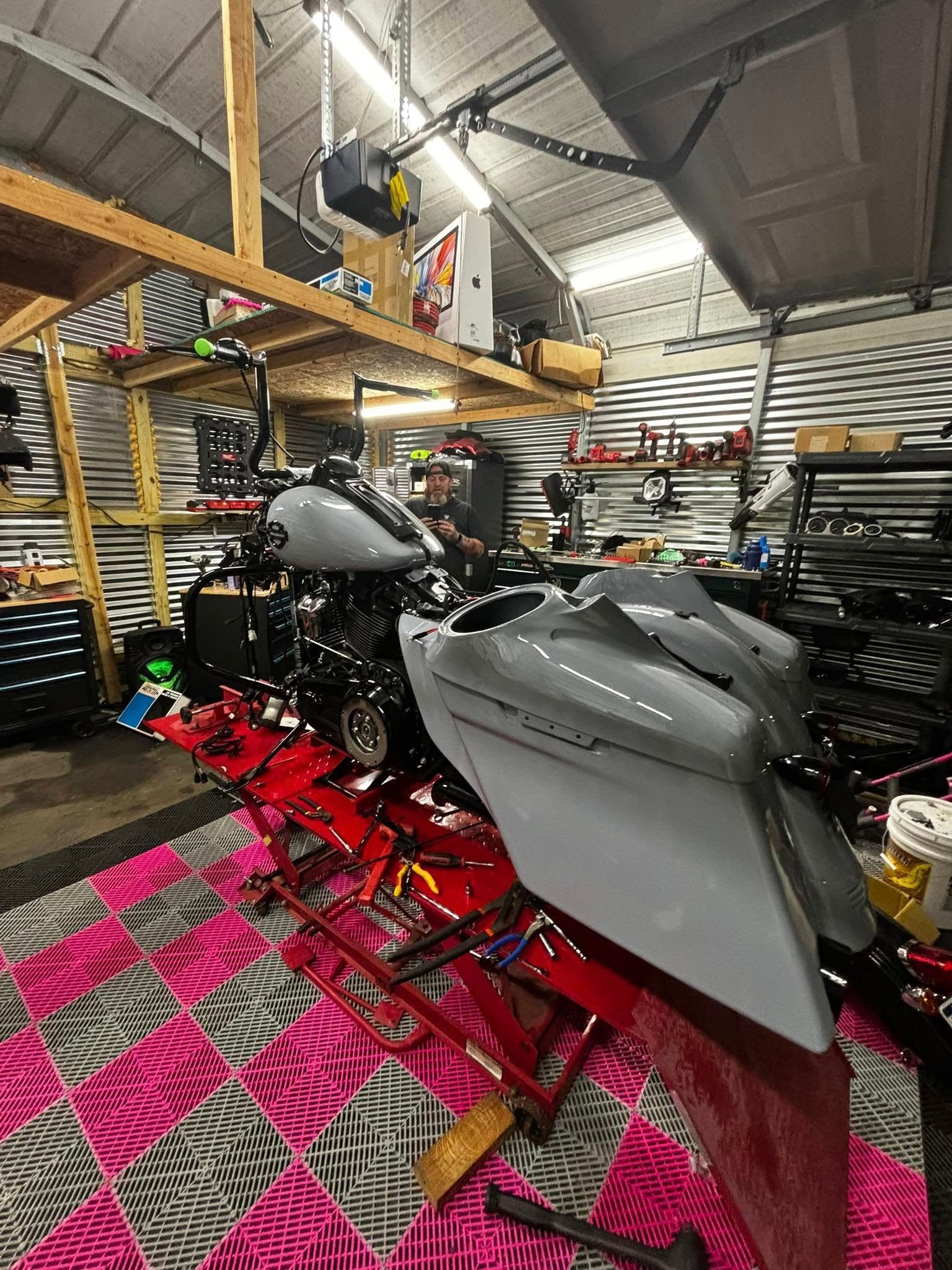 Motorcycle on a lift in a garage with tools and a loft; pink and black checkered floor.