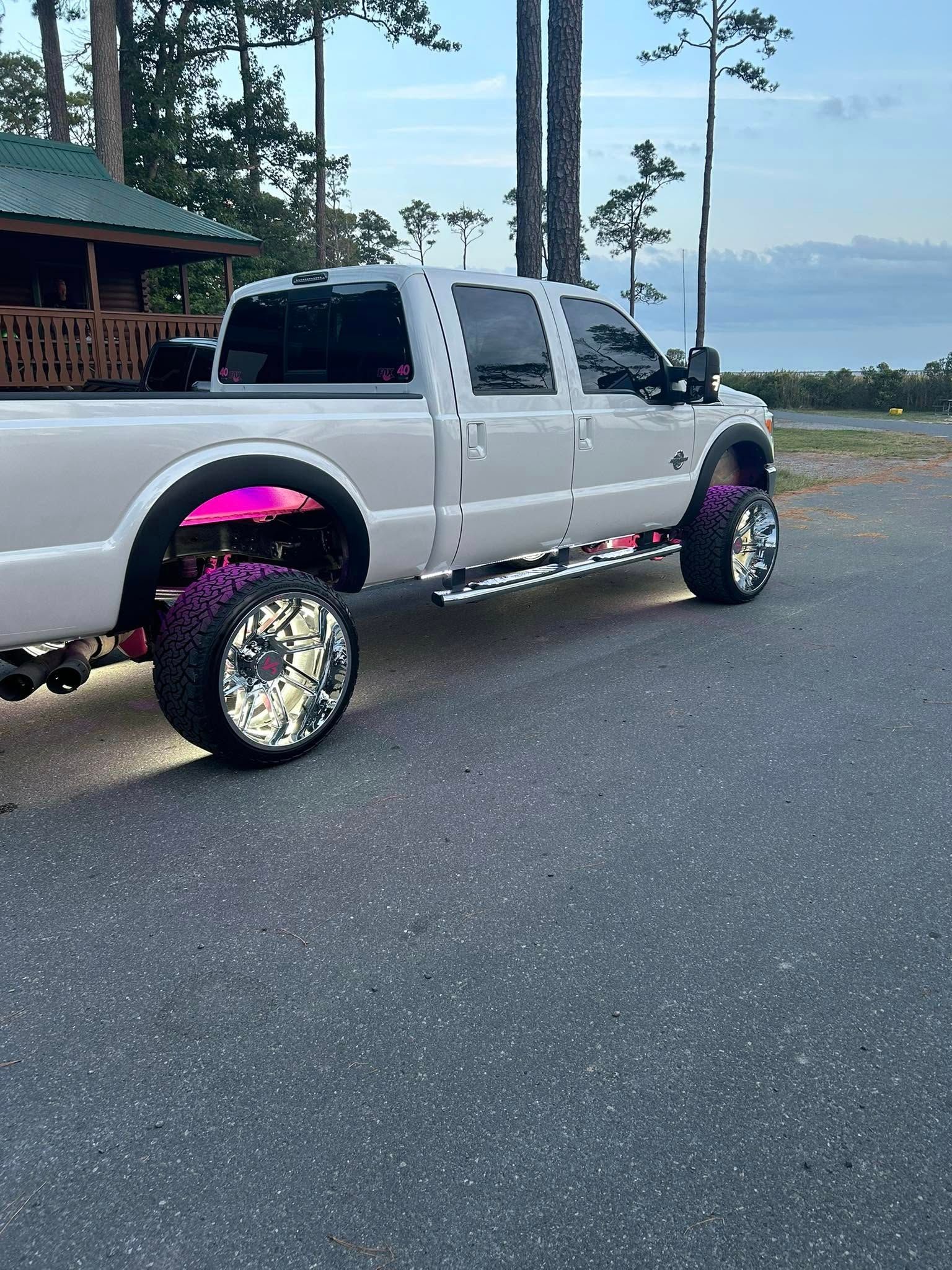 White truck with custom magenta and purple wheel lighting parked on asphalt.