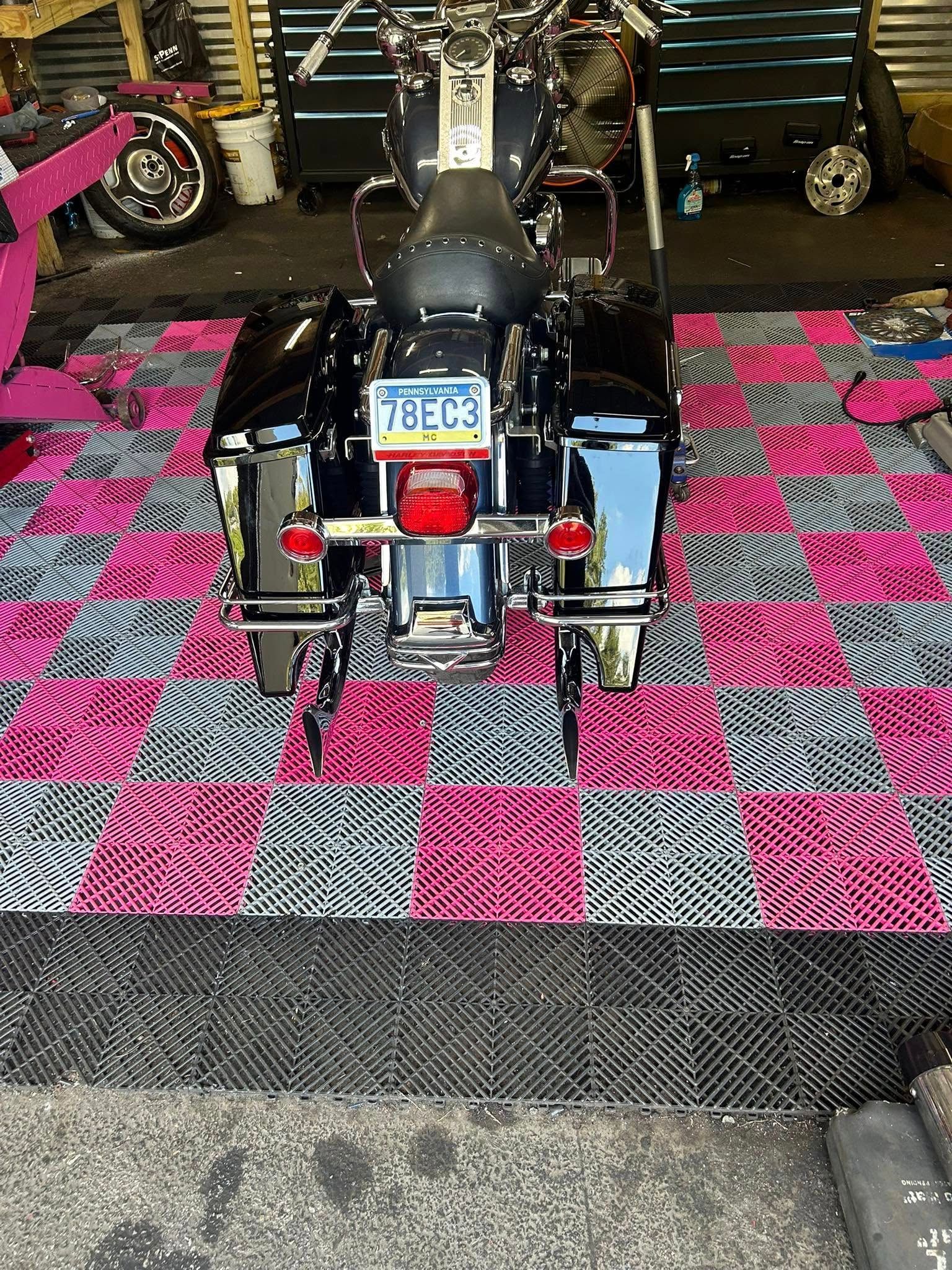 Black motorcycle with saddlebags on a checkered pink/gray floor. Garage setting.