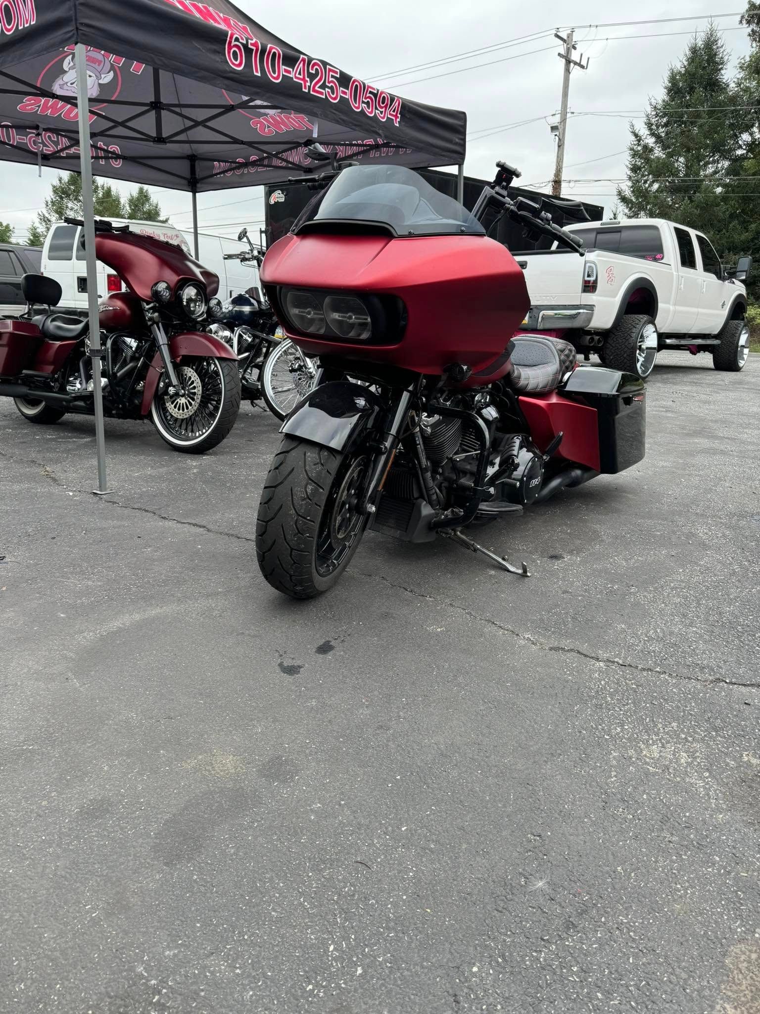 Red motorcycle parked on pavement, under a canopy. Other motorcycles and a white truck in the background.