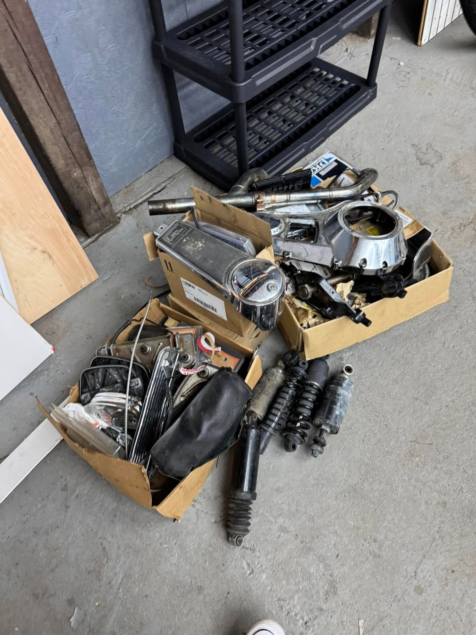 Two cardboard boxes filled with motorcycle parts on a concrete floor next to a storage shelf.