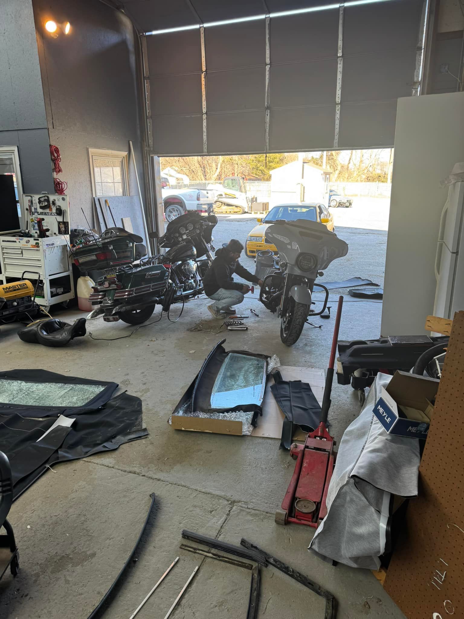 A person working on a motorcycle inside a garage with car parts and tools.