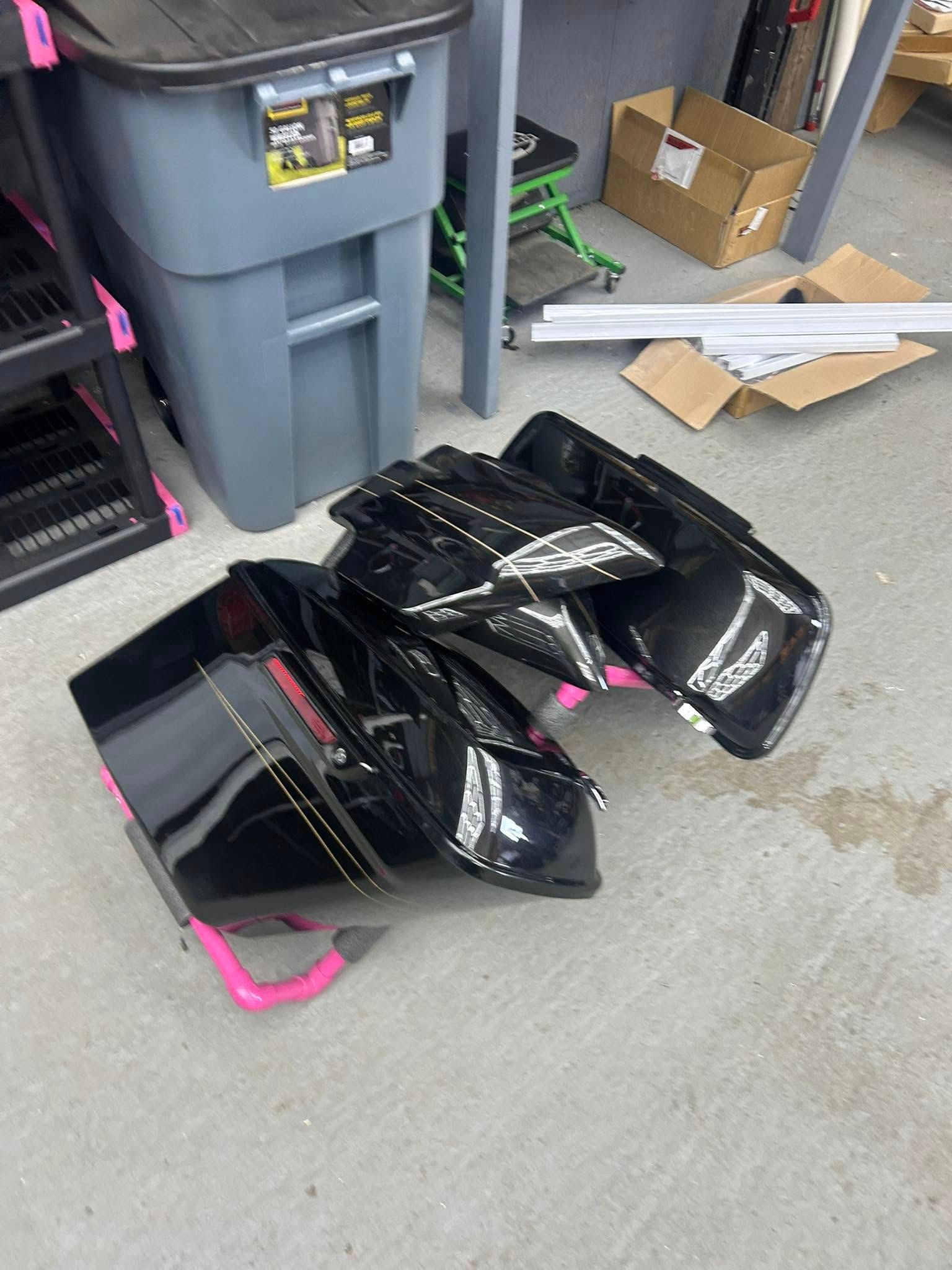 Black motorcycle saddlebags on a garage floor, leaning against a pink stand.