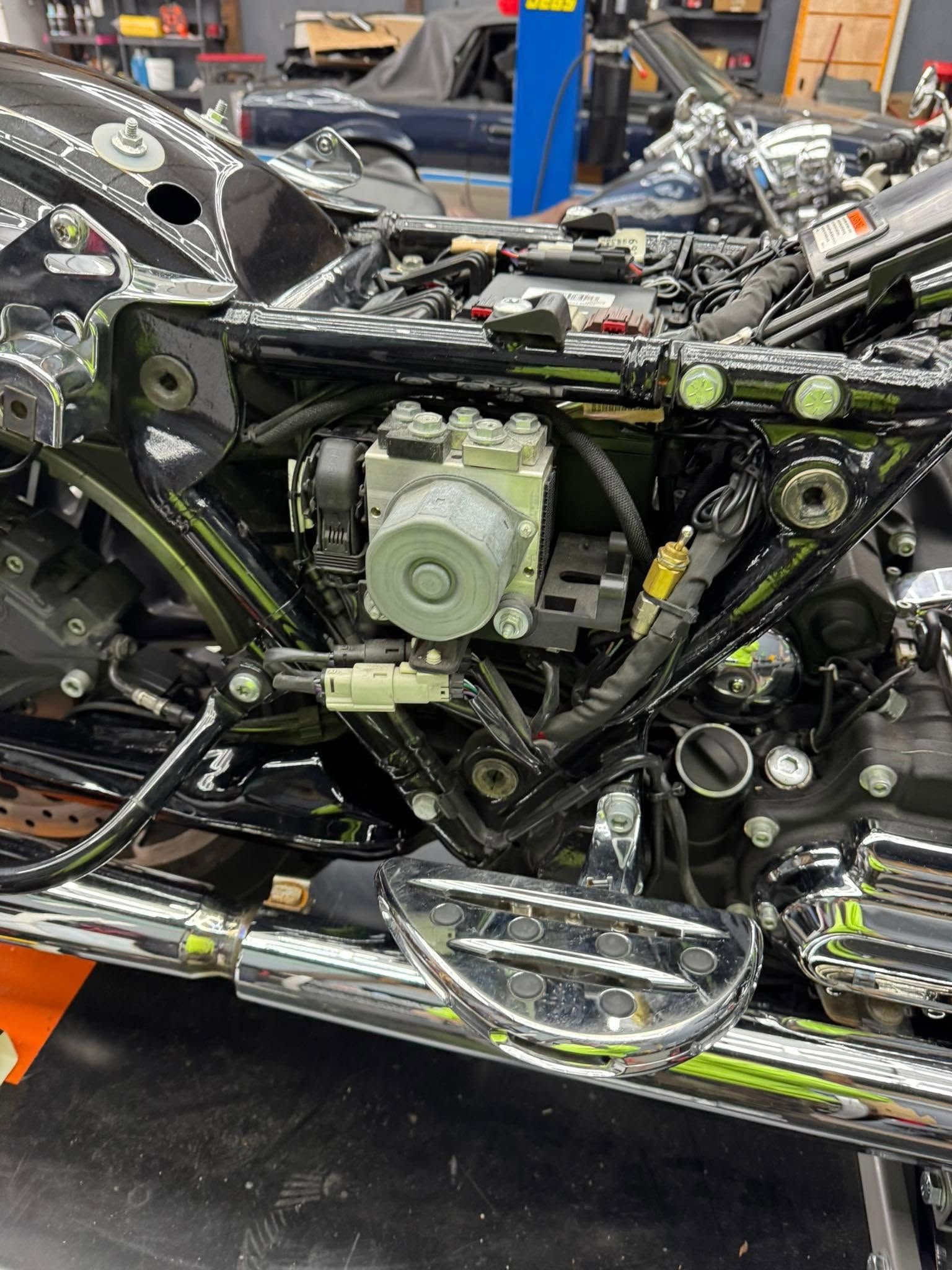 Motorcycle frame with ABS module and wiring exposed, in a shop setting.