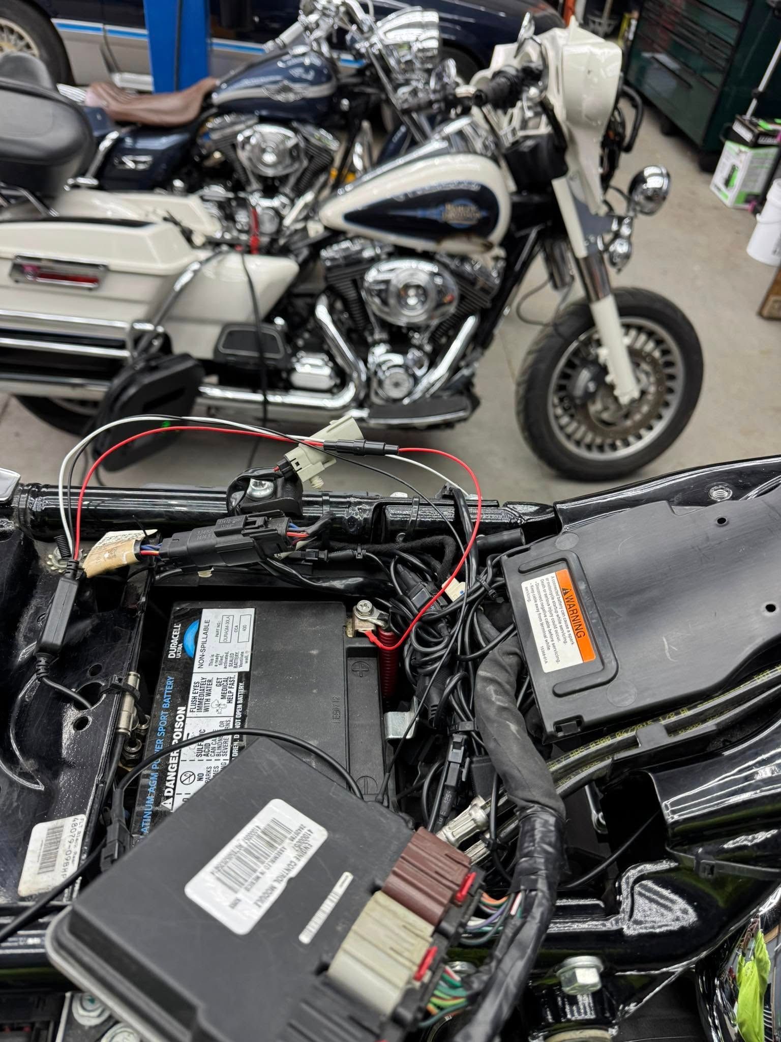 Motorcycle with open seat, wires exposed; another bike in background.