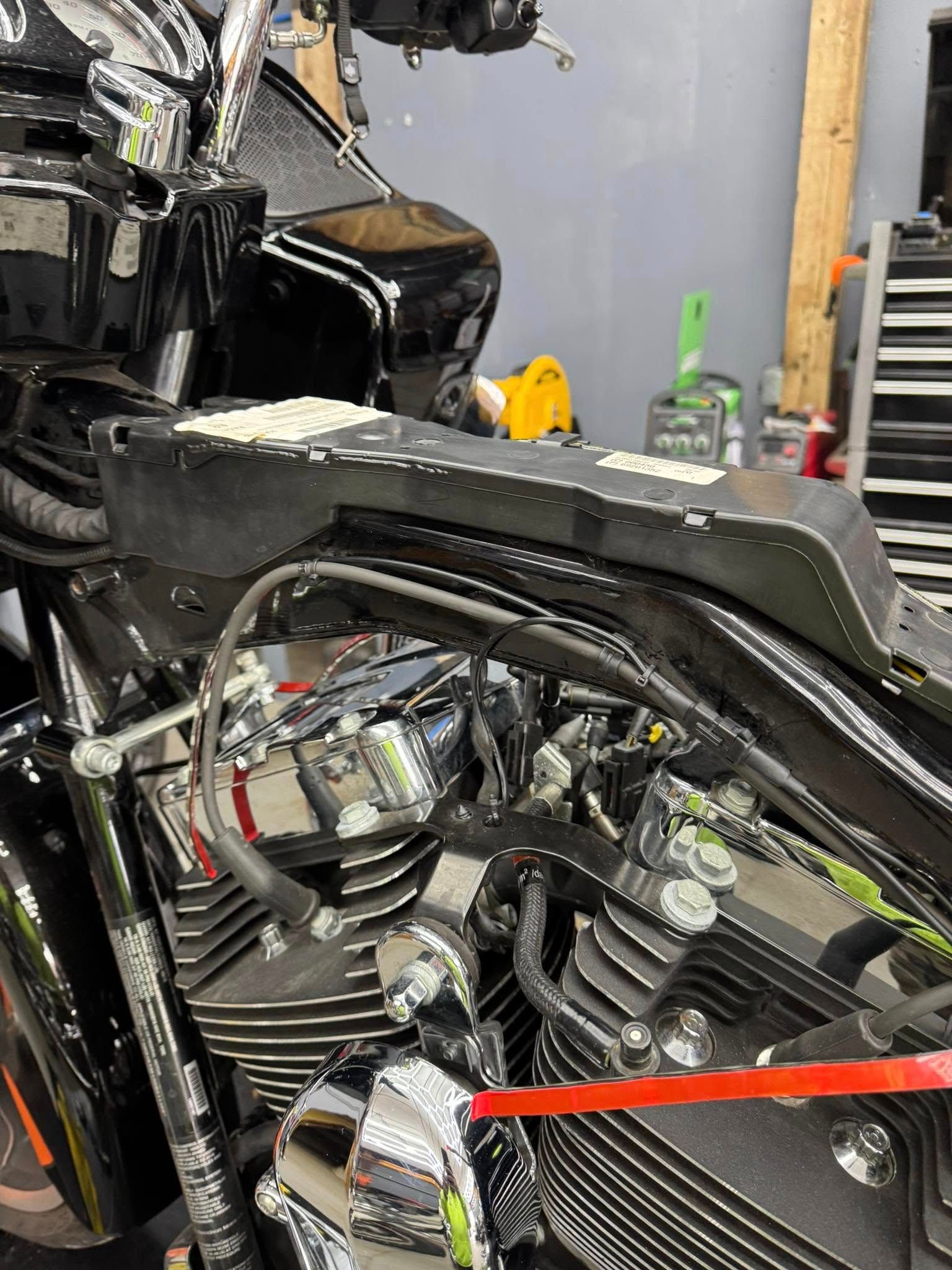 Black motorcycle engine and seat detail. Chrome accents, red tape, and workshop background.