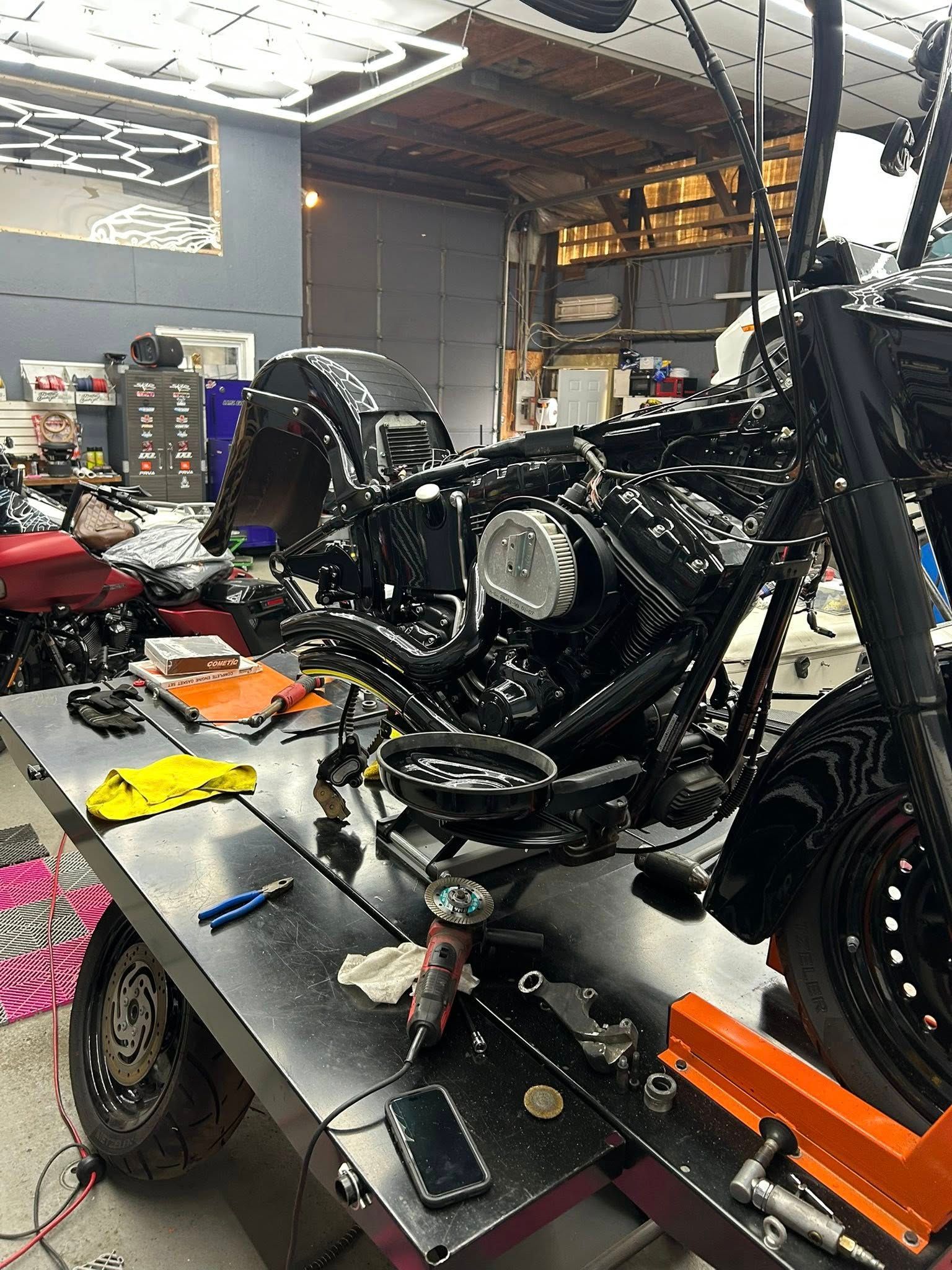 Black motorcycle being worked on in a garage; parts and tools on a workbench.