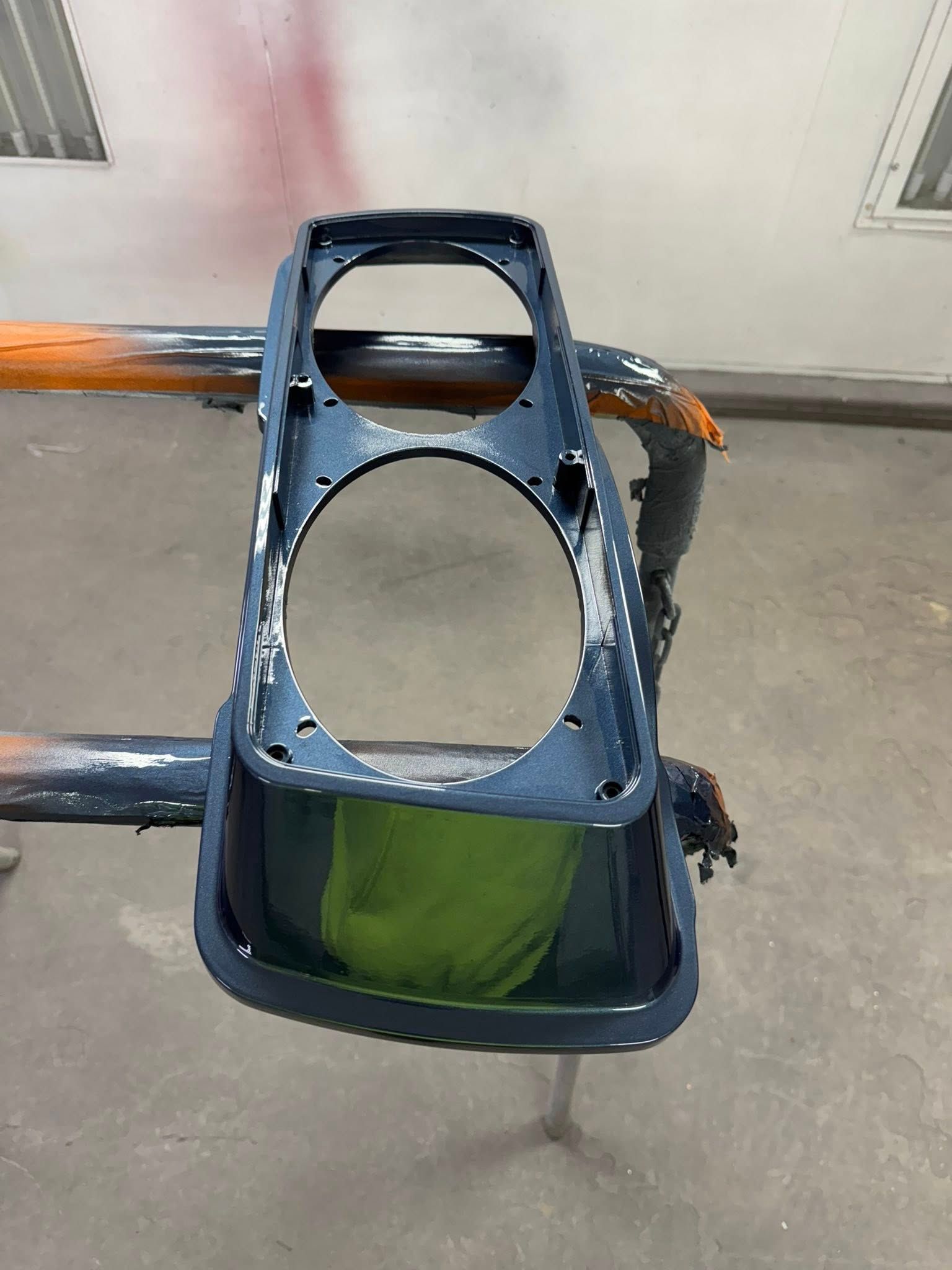Dark blue painted headlight bezel, suspended in a spray booth.