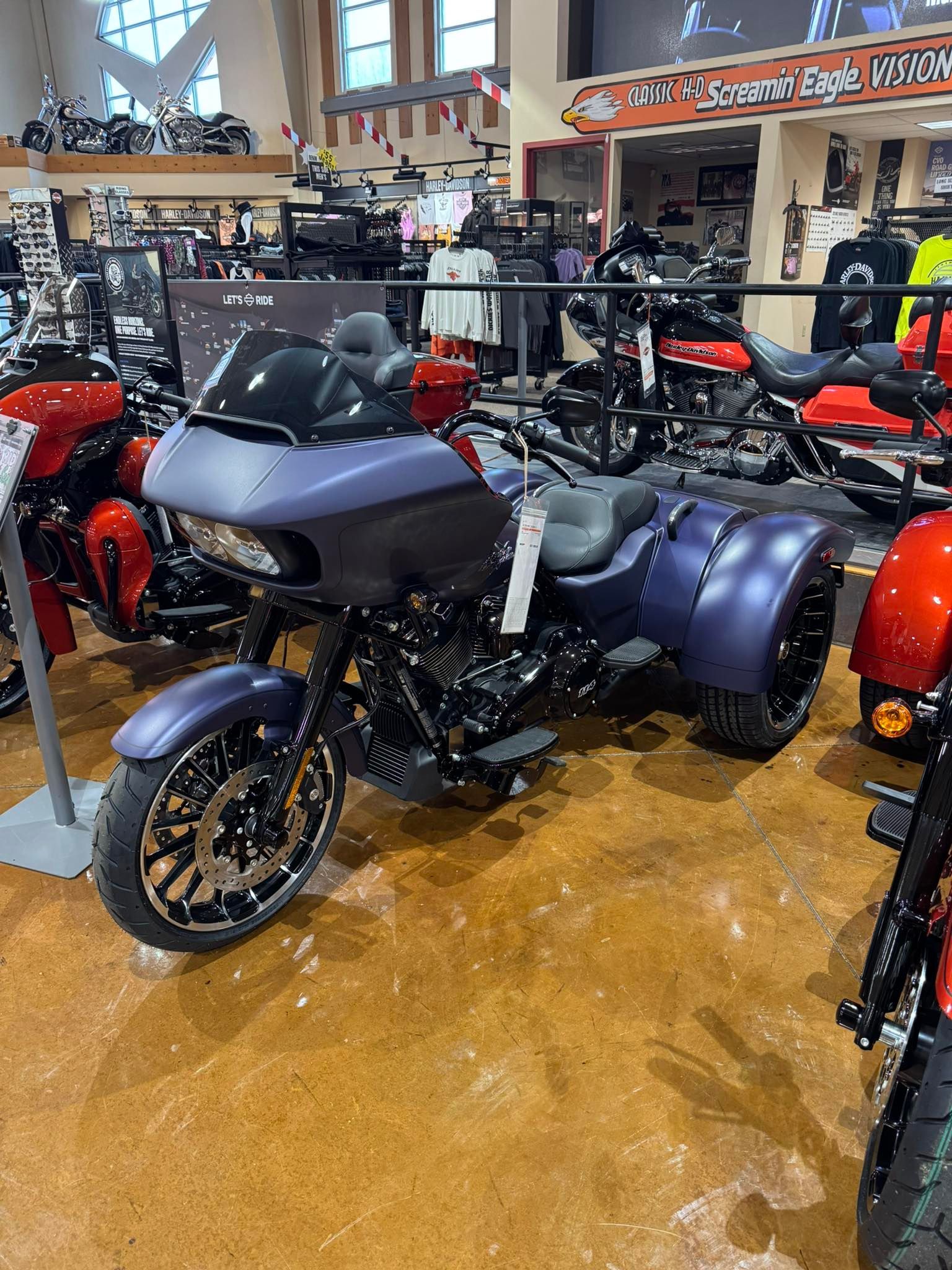 Blue and black Harley-Davidson trike motorcycle on display in a showroom, surrounded by other bikes and merchandise.