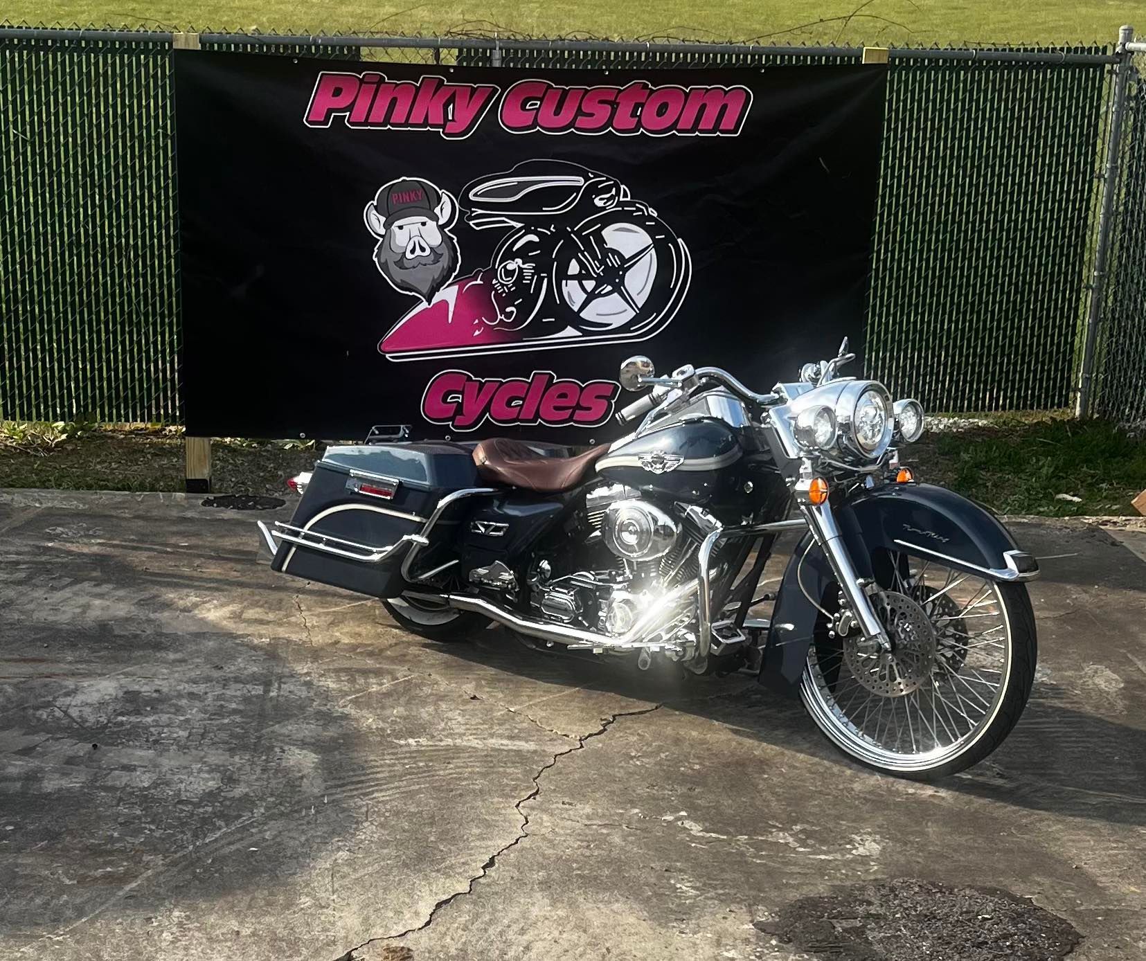 Black custom motorcycle in front of a Pinky Custom Cycles banner.