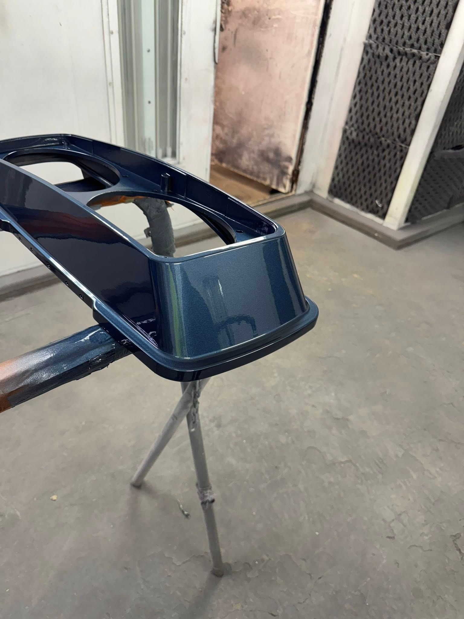 Dark blue painted car part on a stand in a paint booth.