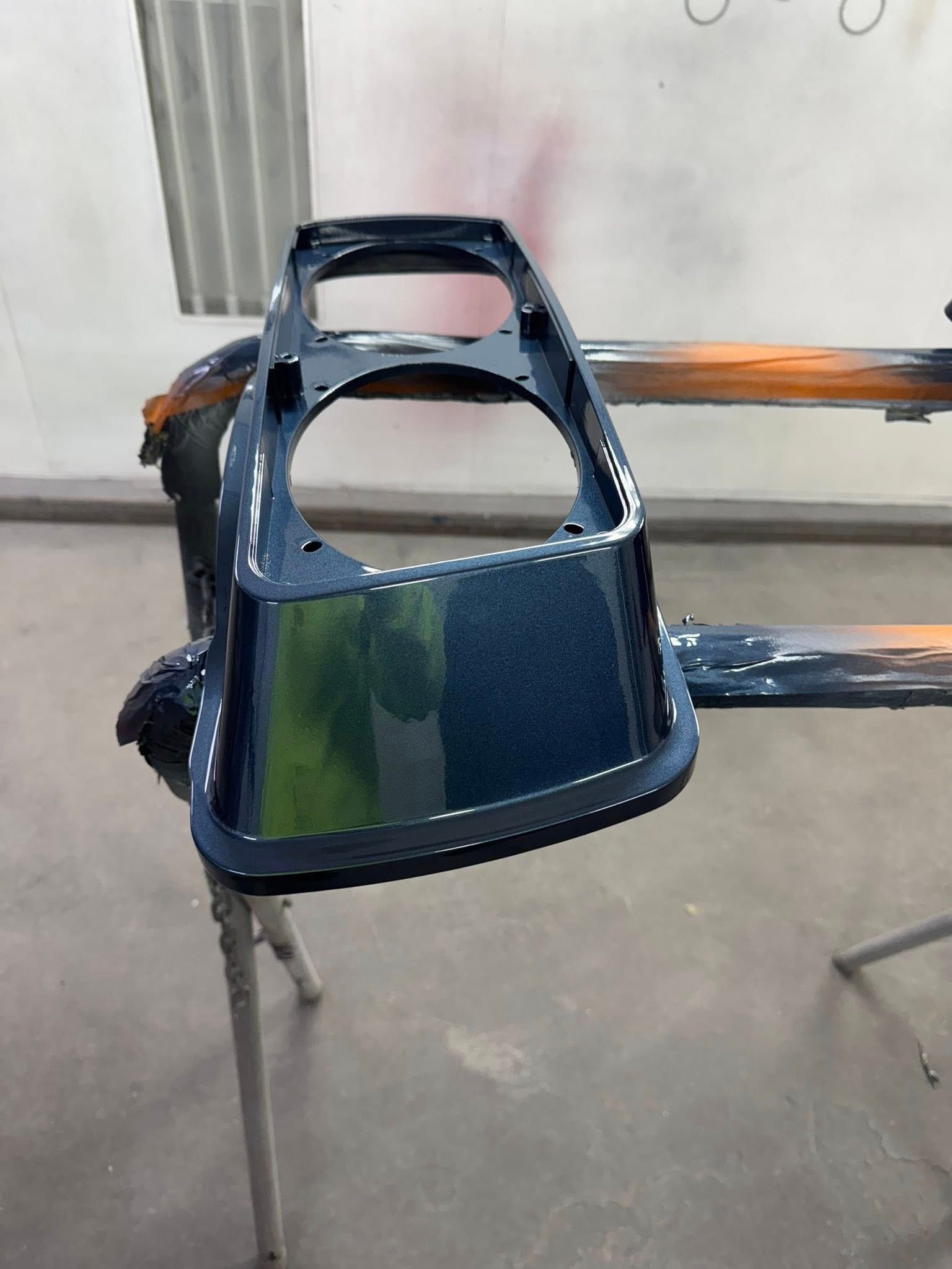 Dark blue car part, possibly dashboard, freshly painted in a workshop.