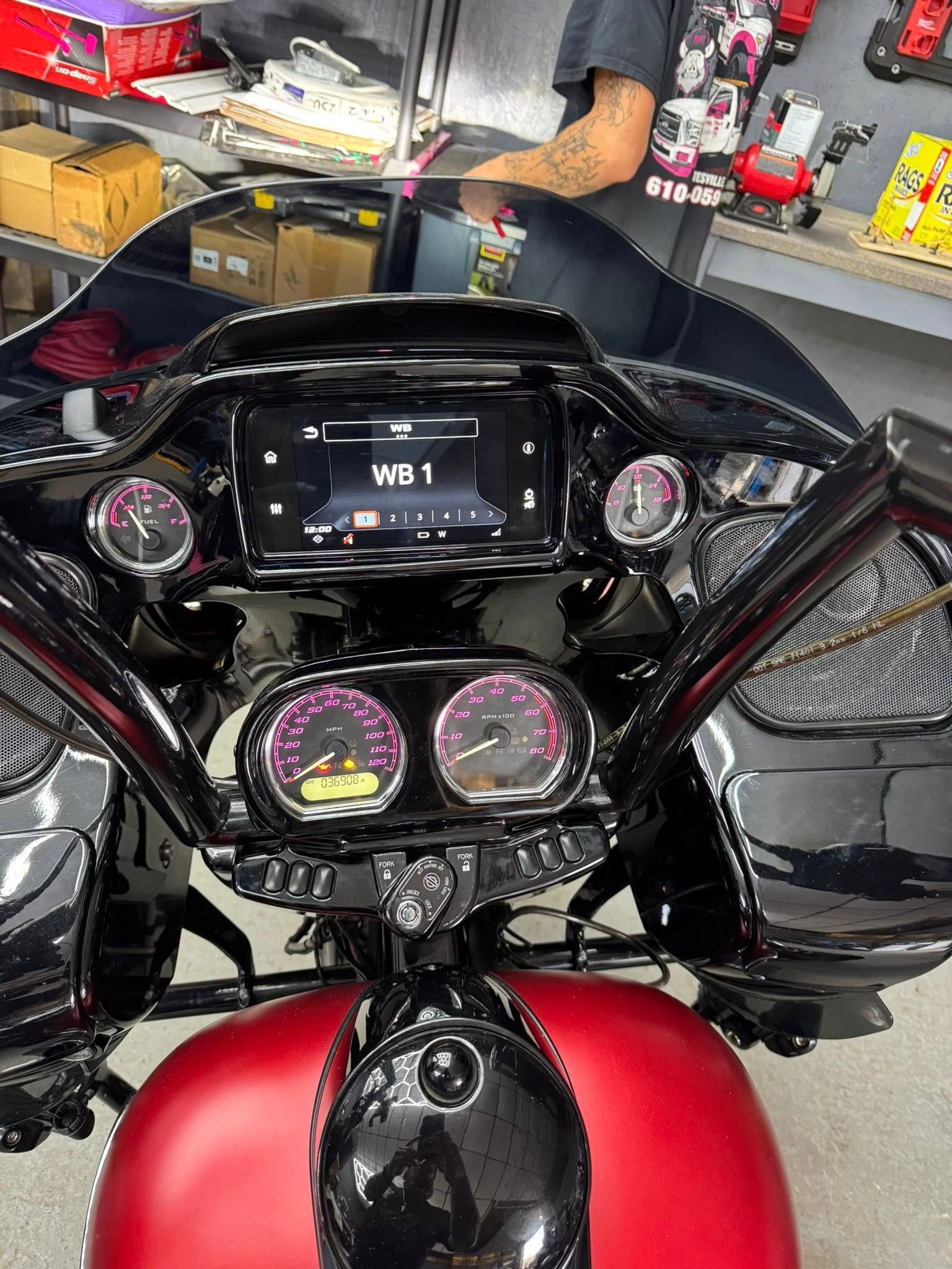 Black and red motorcycle dashboard with gauges, screen, and a person in the background.