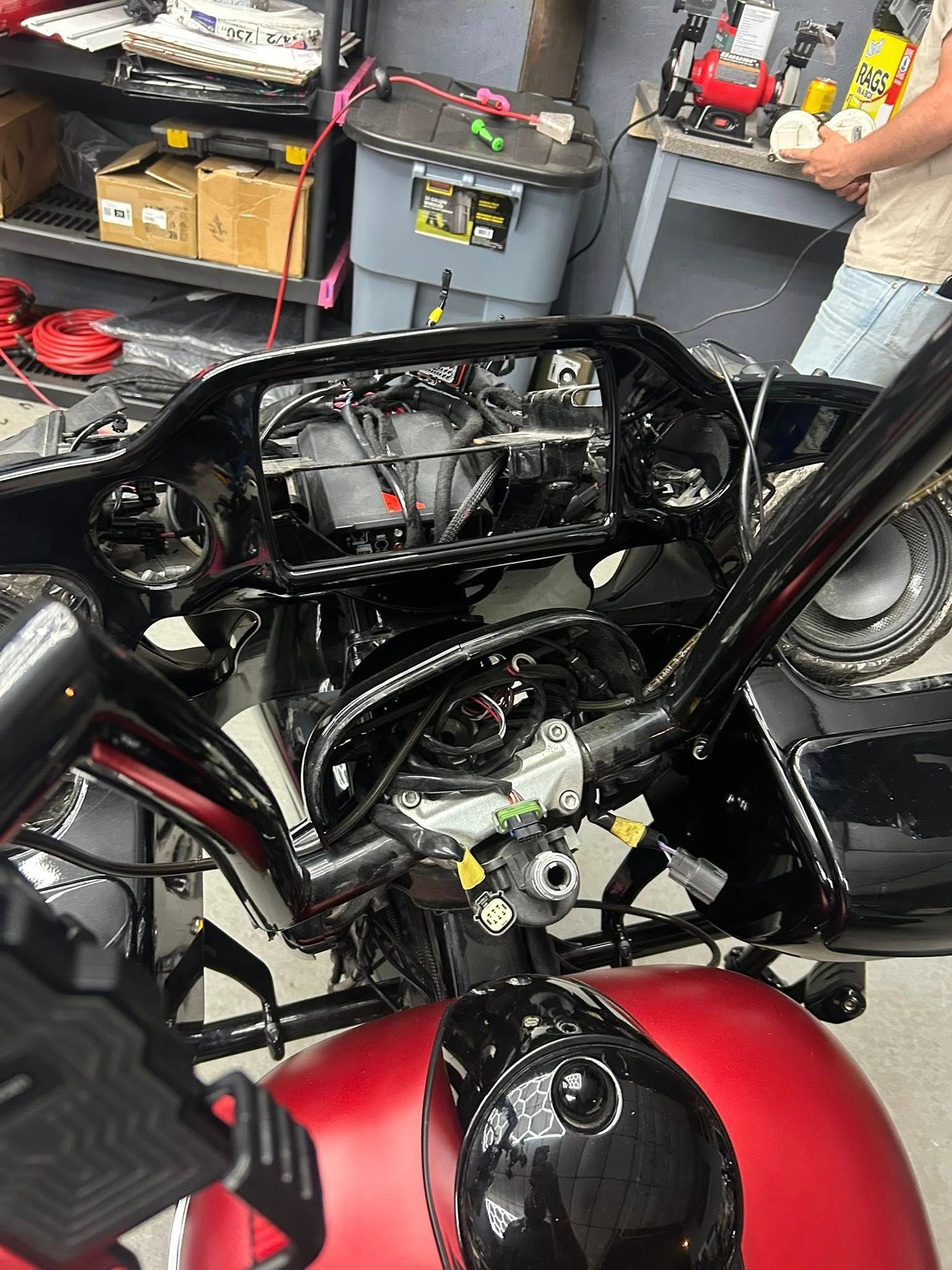 Motorcycle dashboard disassembled, with exposed wiring and black handlebars, in a garage.