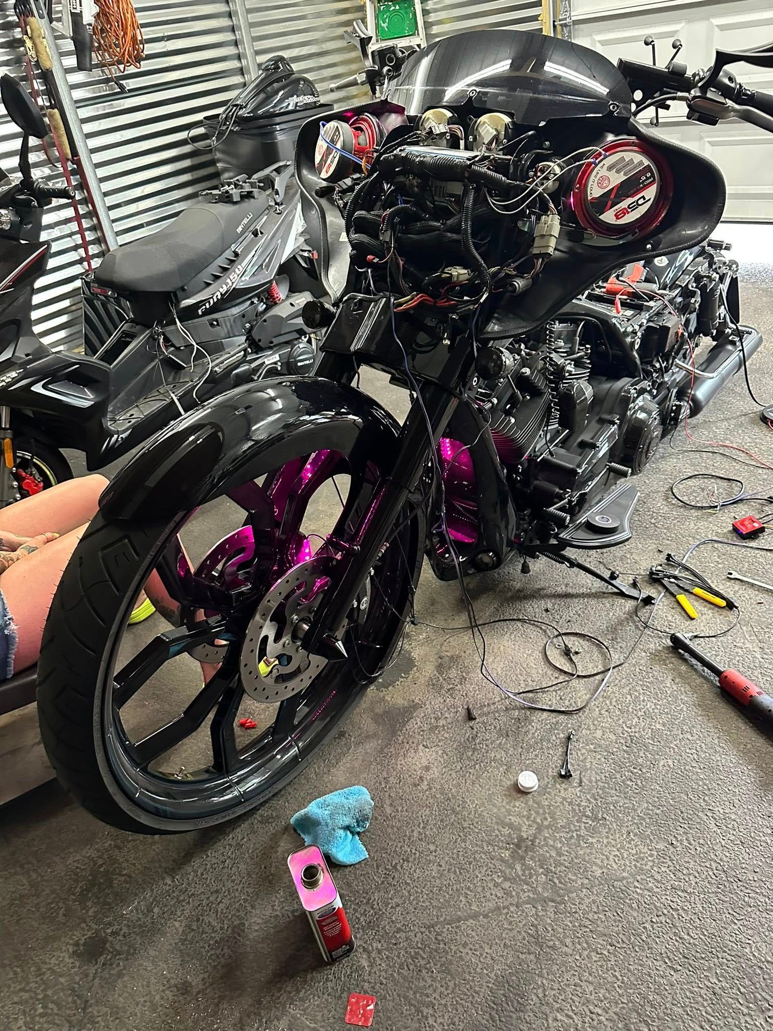 Black custom motorcycle with pink accents being worked on in a garage.