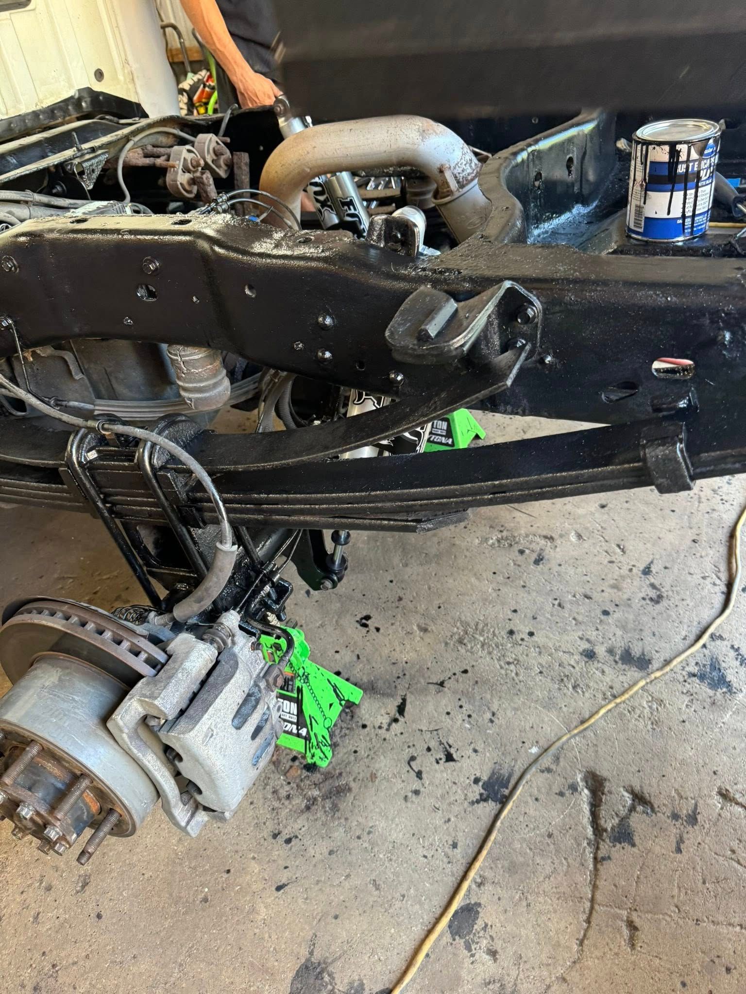 Truck frame being worked on, black paint, rear suspension visible, brake assembly, concrete floor.