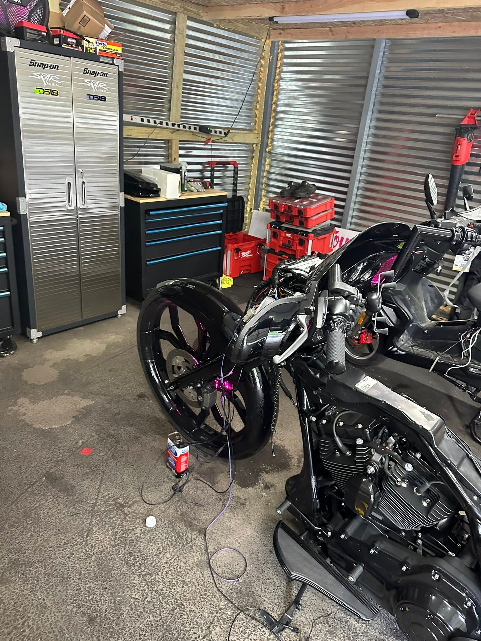 Motorcycles in a garage with tools and storage cabinets. Shiny black vehicles, corrugated metal walls.