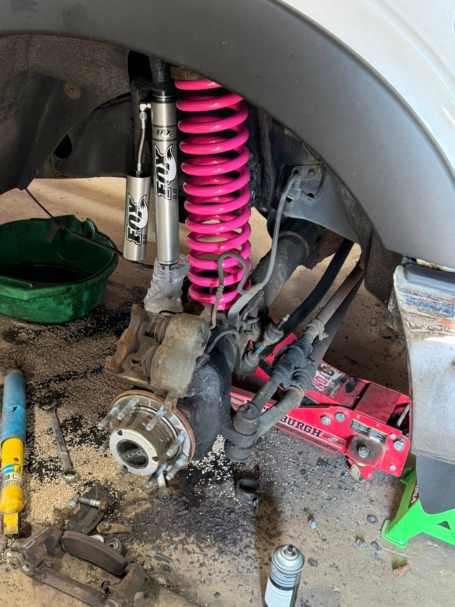 Vehicle suspension being worked on. Pink coil spring, Fox shock absorber, tools visible.