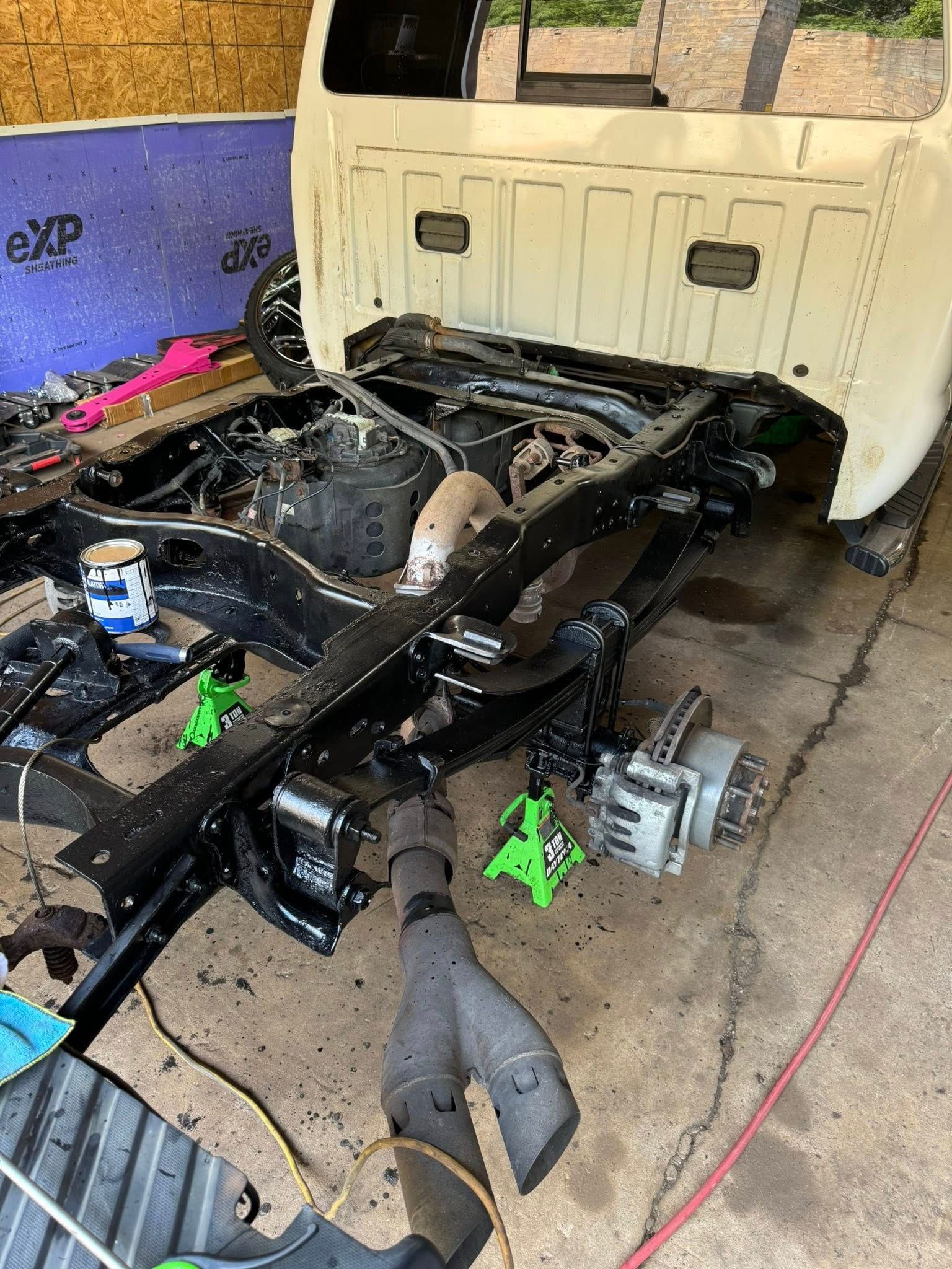 Black truck chassis with white bed in a garage, supported by jack stands.