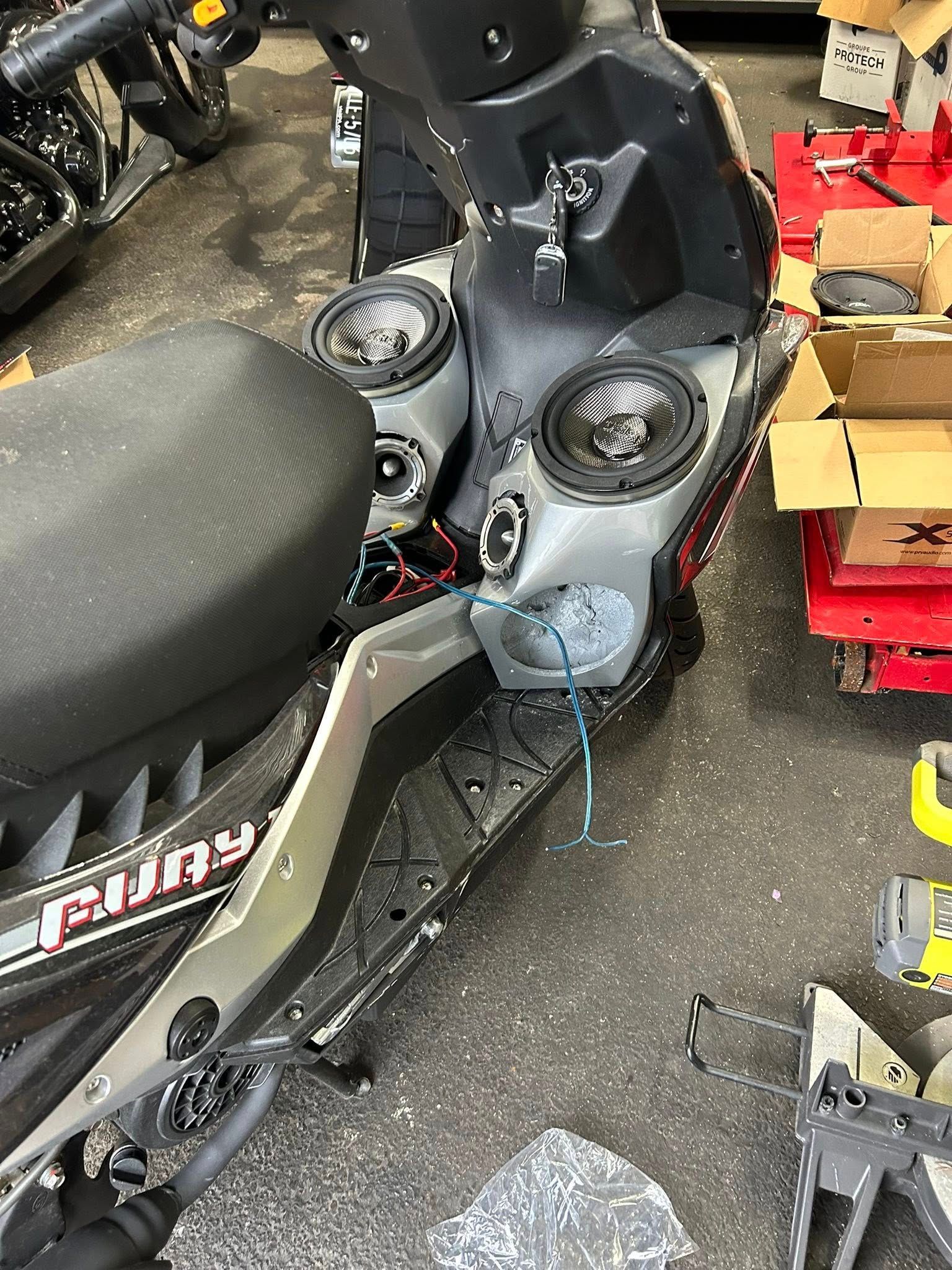 Scooter modified with multiple speakers mounted on the front. Gray and black.