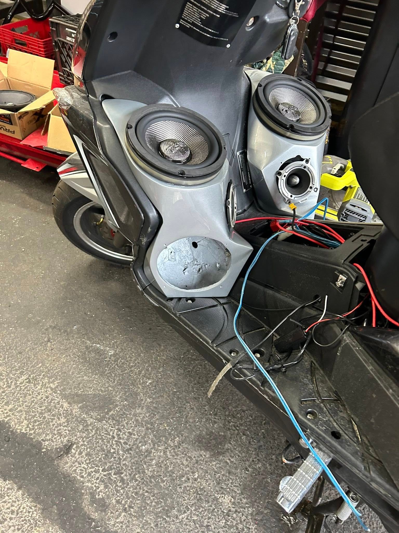 Motor scooter with speakers installed, wires exposed, in a garage setting.