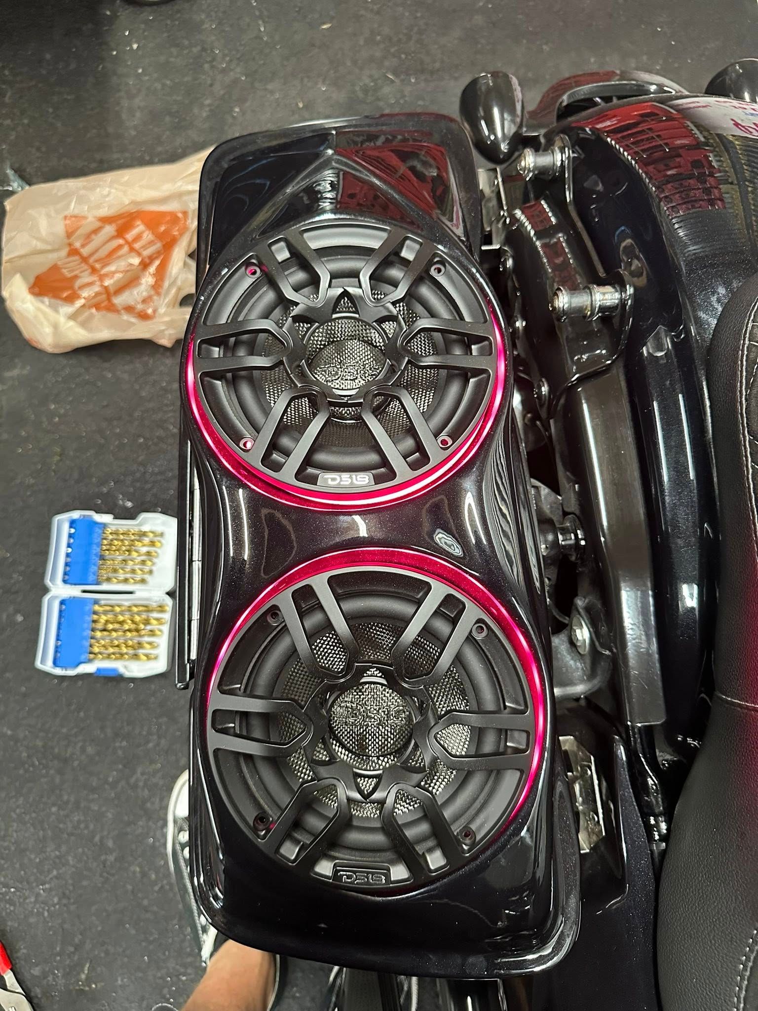 Motorcycle saddlebag with two round speakers, black with red accents.