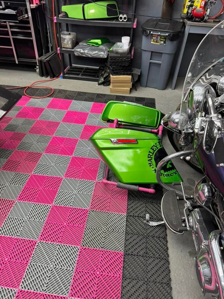 Pink and gray checkered floor in garage with a lime green motorcycle, storage shelves, and trash bin.