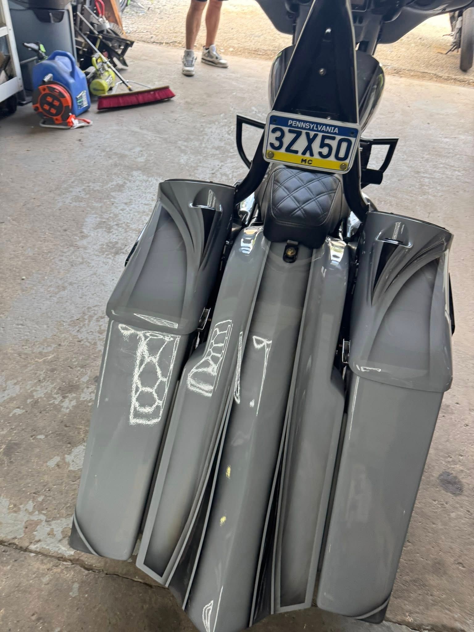 Gray motorcycle with custom saddlebags, parked outdoors, license plate visible.
