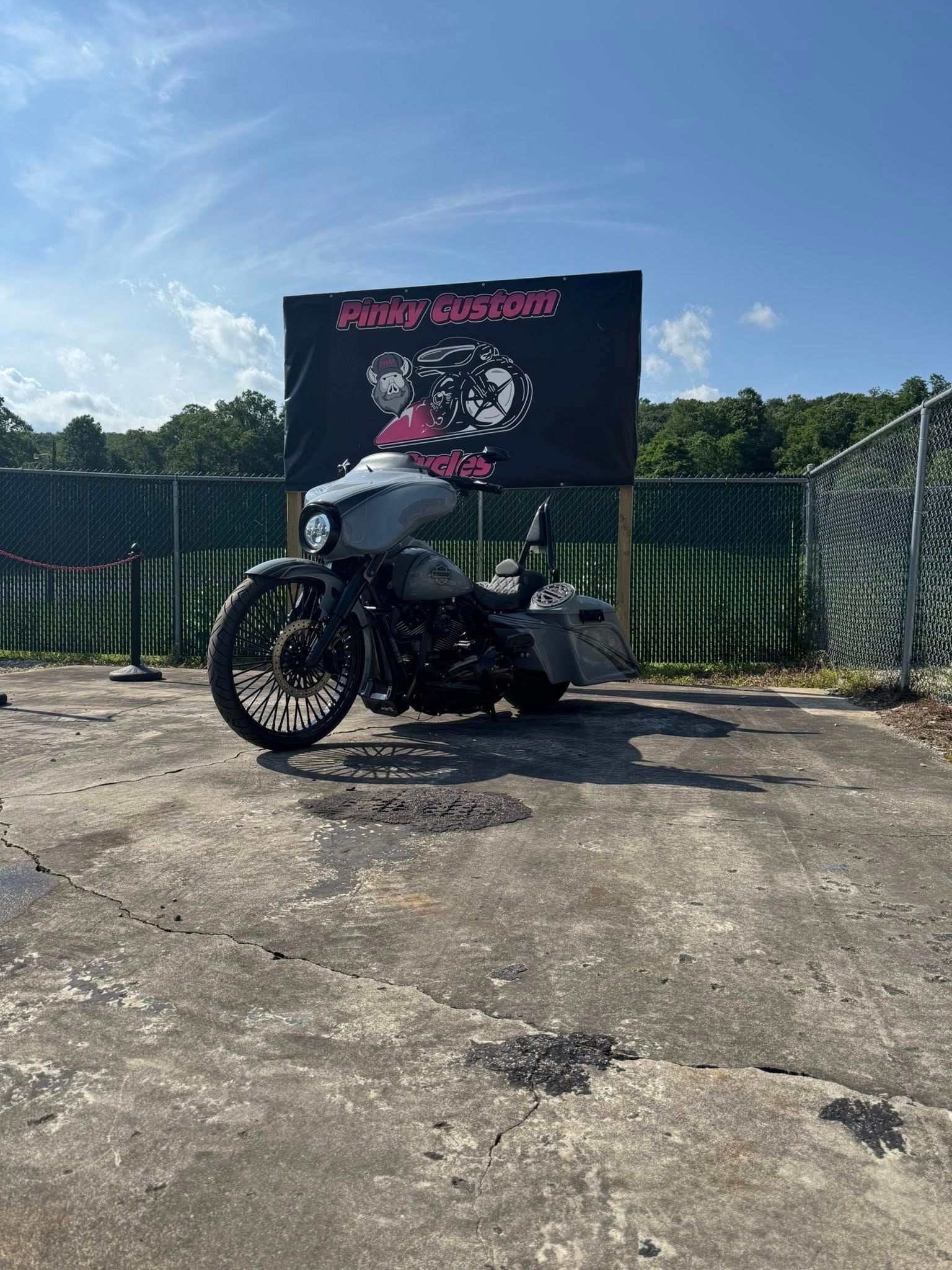 Motorcycle parked in front of a sign with pink writing against a black background. Concrete parking area.