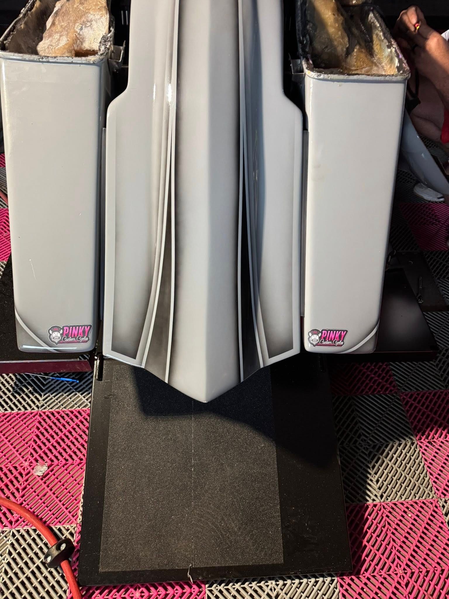 Gray motorcycle saddlebags and rear fender, on a black pad with pink carpet.