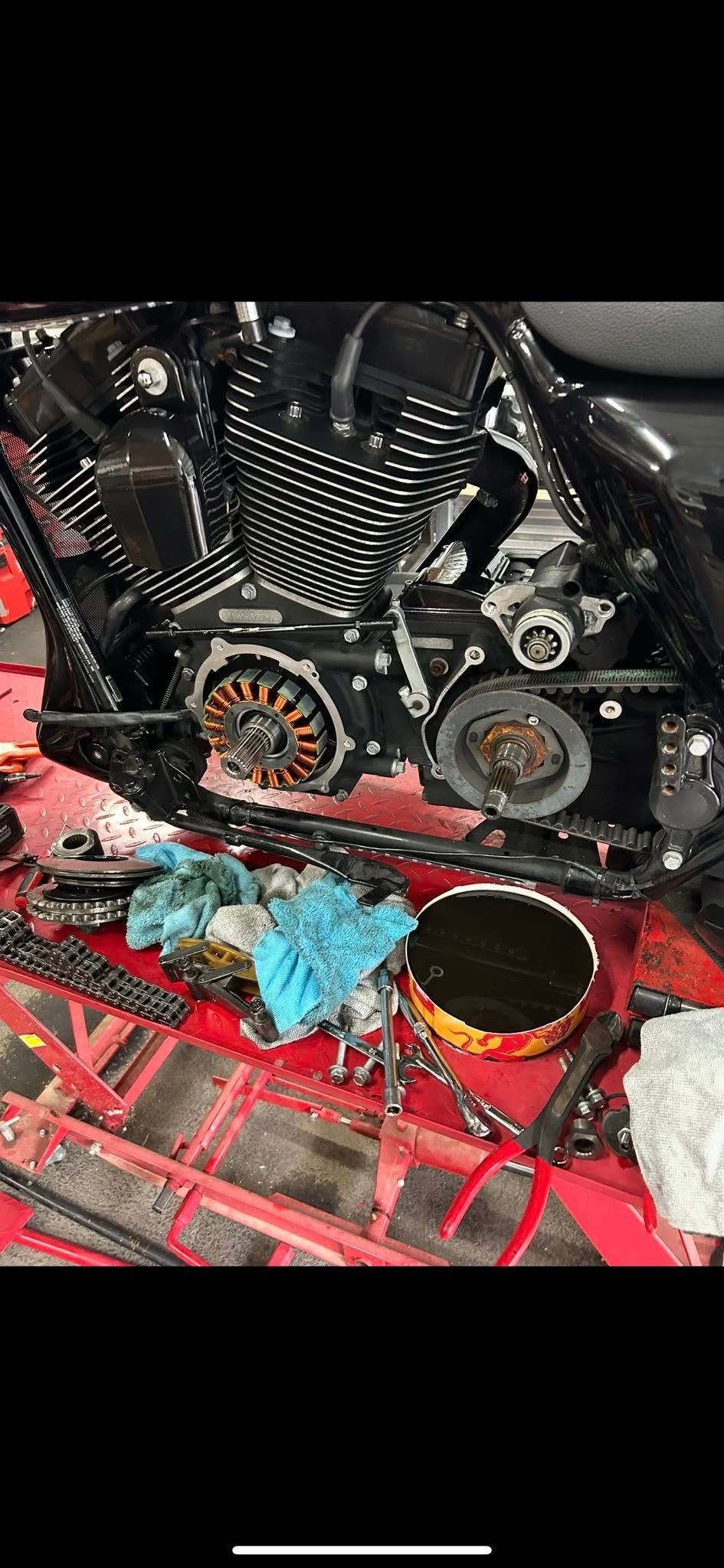 Motorcycle engine with parts removed, tools and rags on a red work surface.