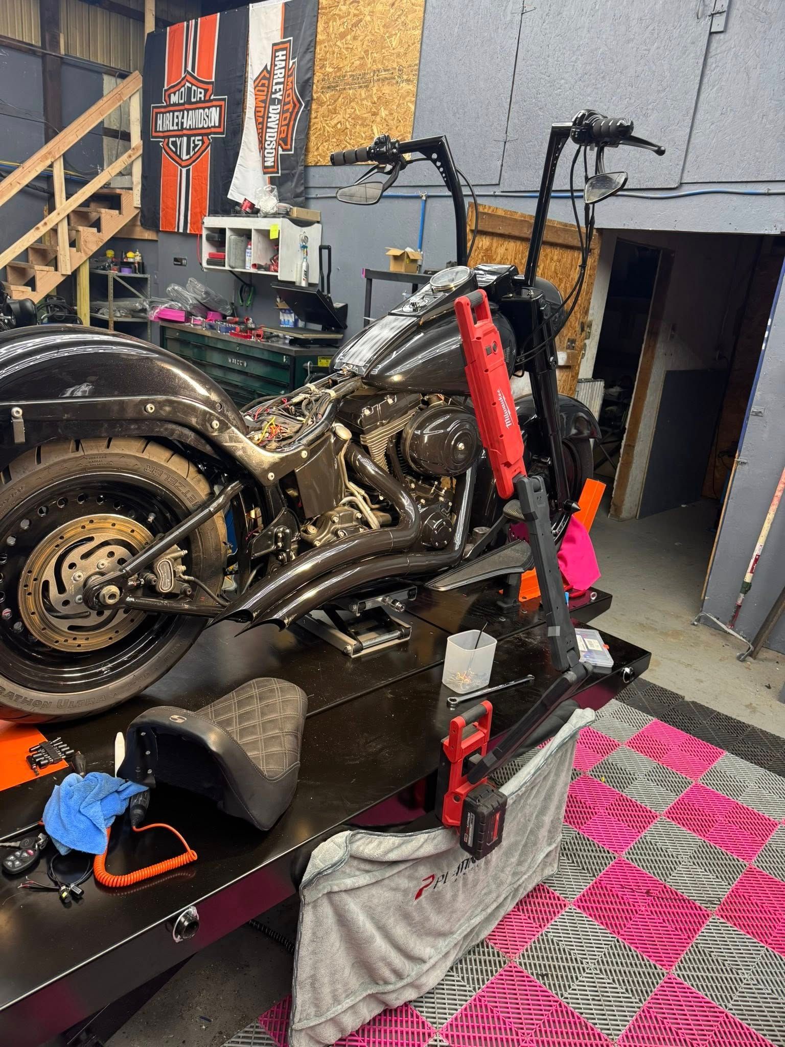 Black Harley-Davidson motorcycle on a lift in a garage. Tools and parts are visible.