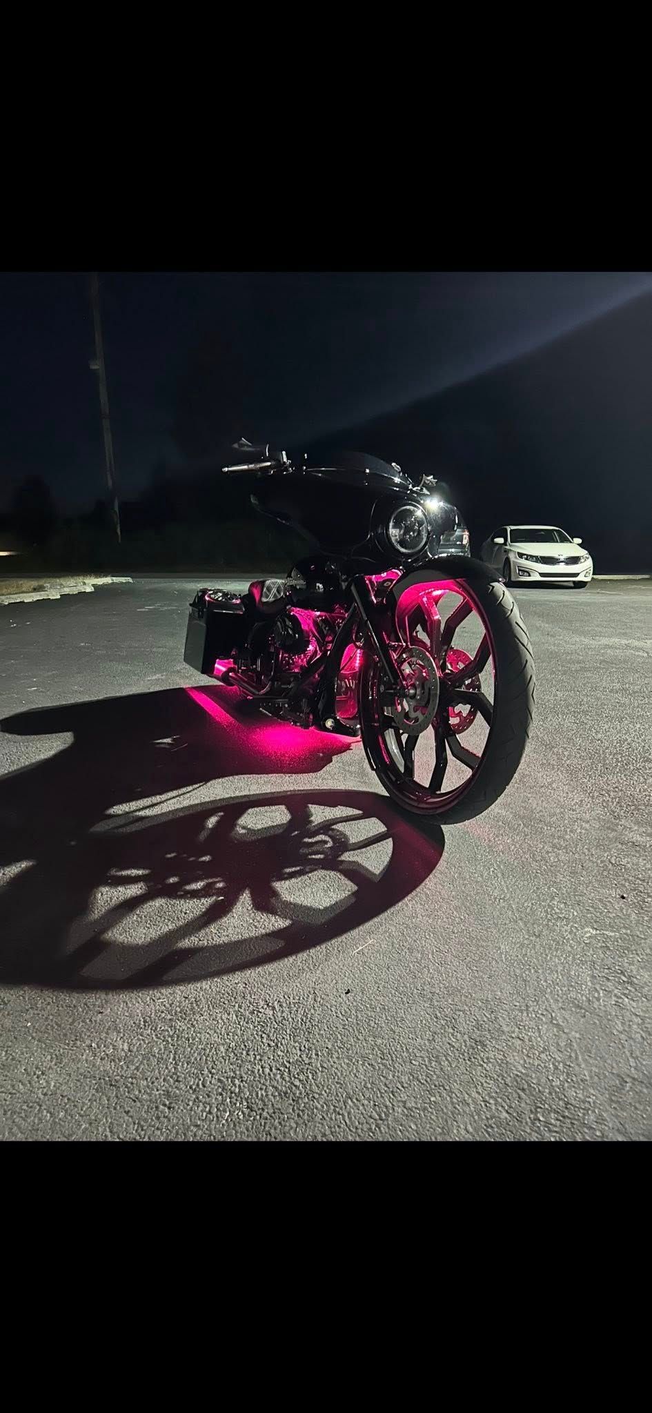 A motorcycle at night with pink neon lights. A car is visible in the background.