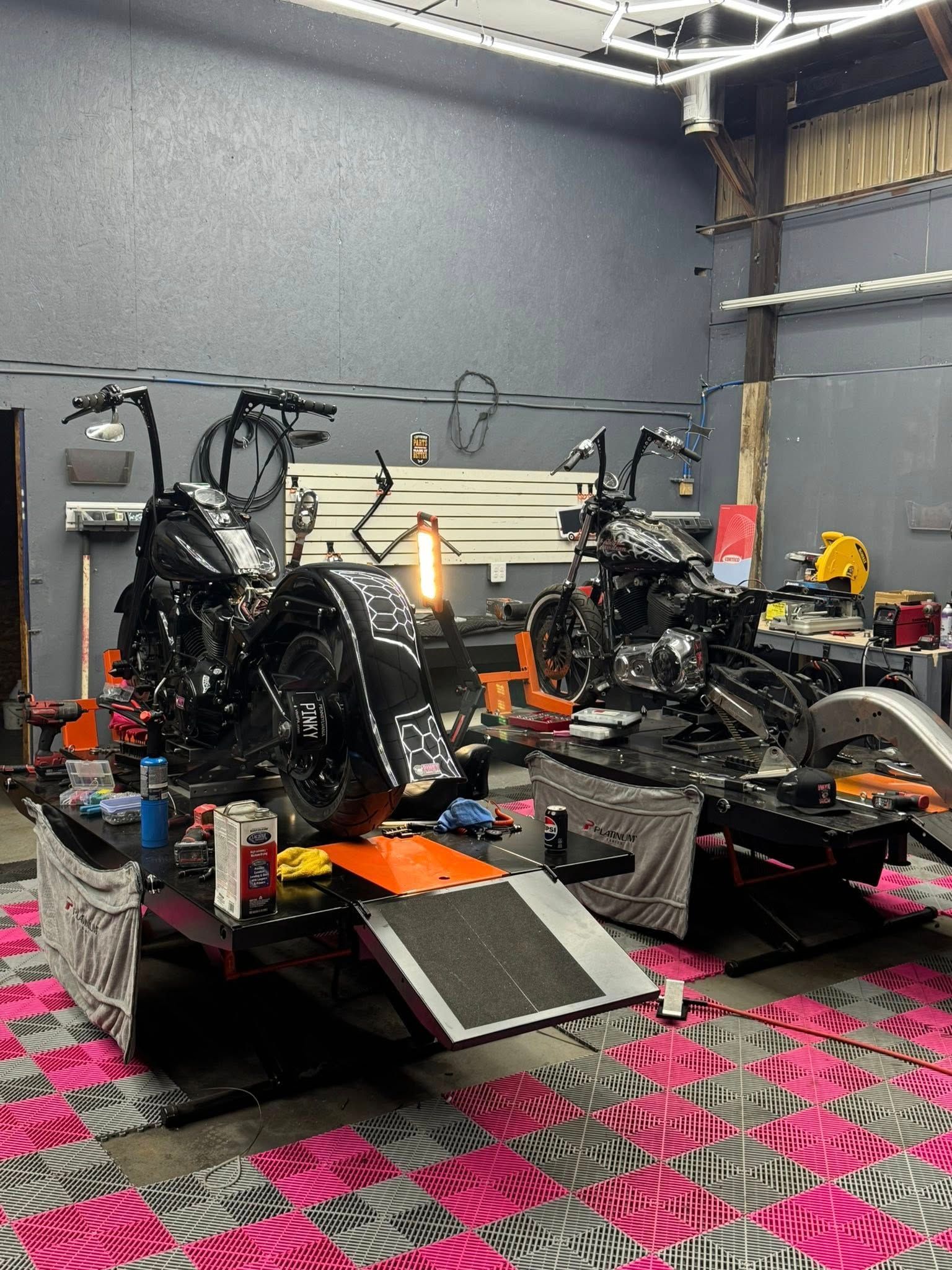 Two black motorcycles on lifts inside a garage, surrounded by tools and equipment.