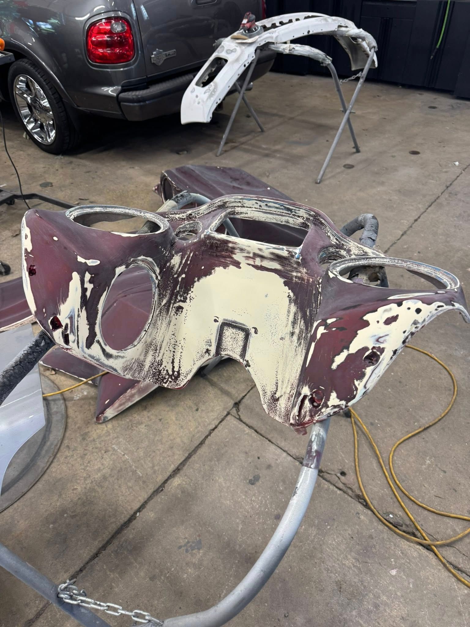 Automotive body panel, partially stripped of paint, on a workbench in a garage.