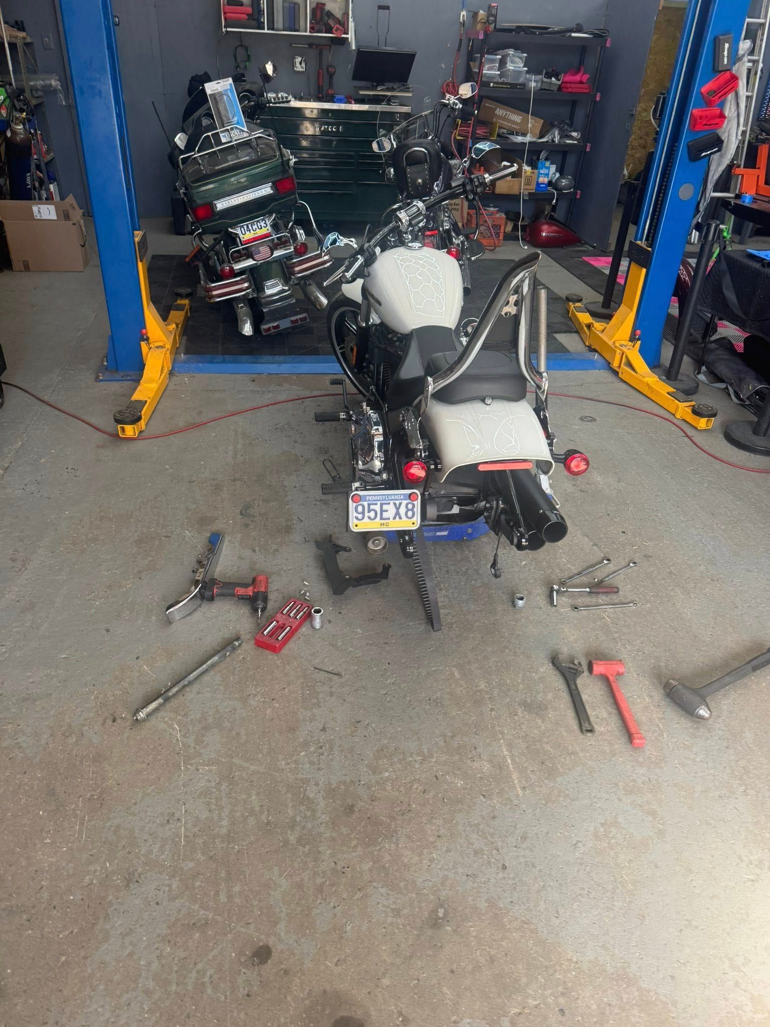 Motorcycles in a garage, one undergoing repair with tools scattered on the floor; another is in the background.