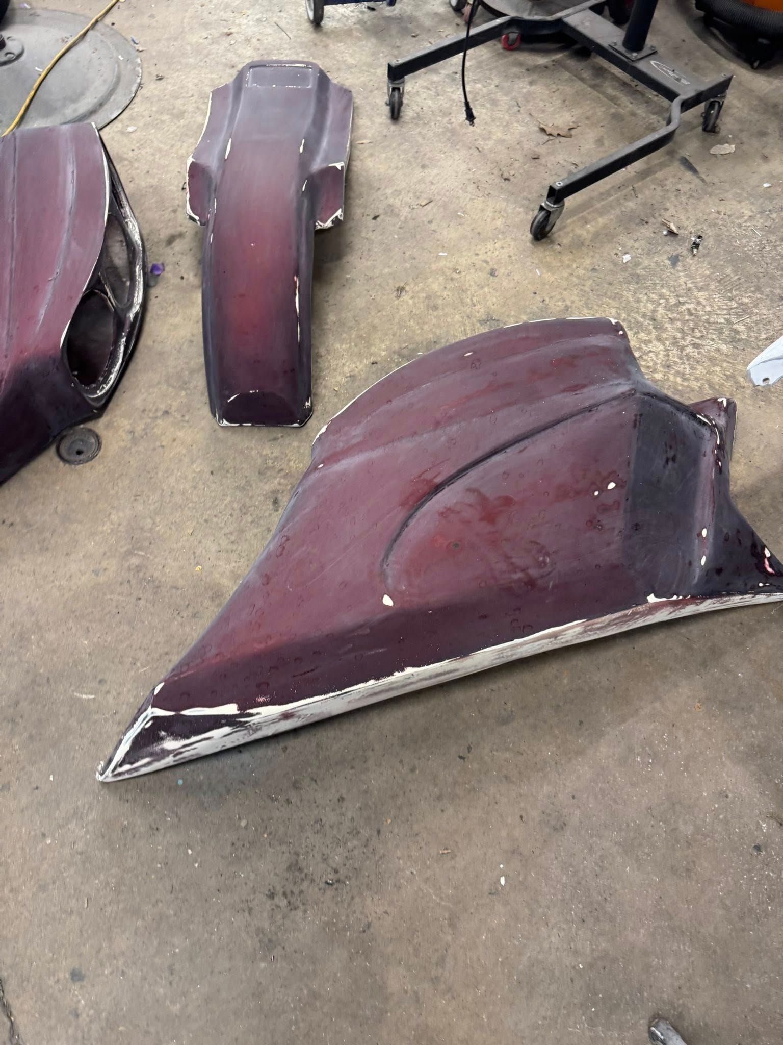 Three maroon car body panels on a shop floor; white edges.
