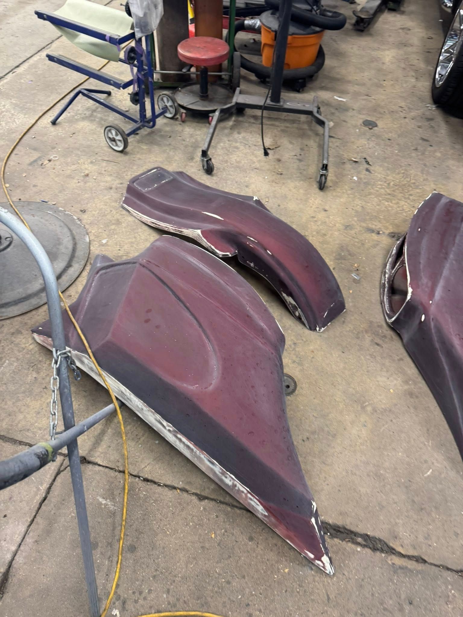 Three automotive body panels, reddish-brown, on a concrete floor in a workshop, possibly being prepped for paint.
