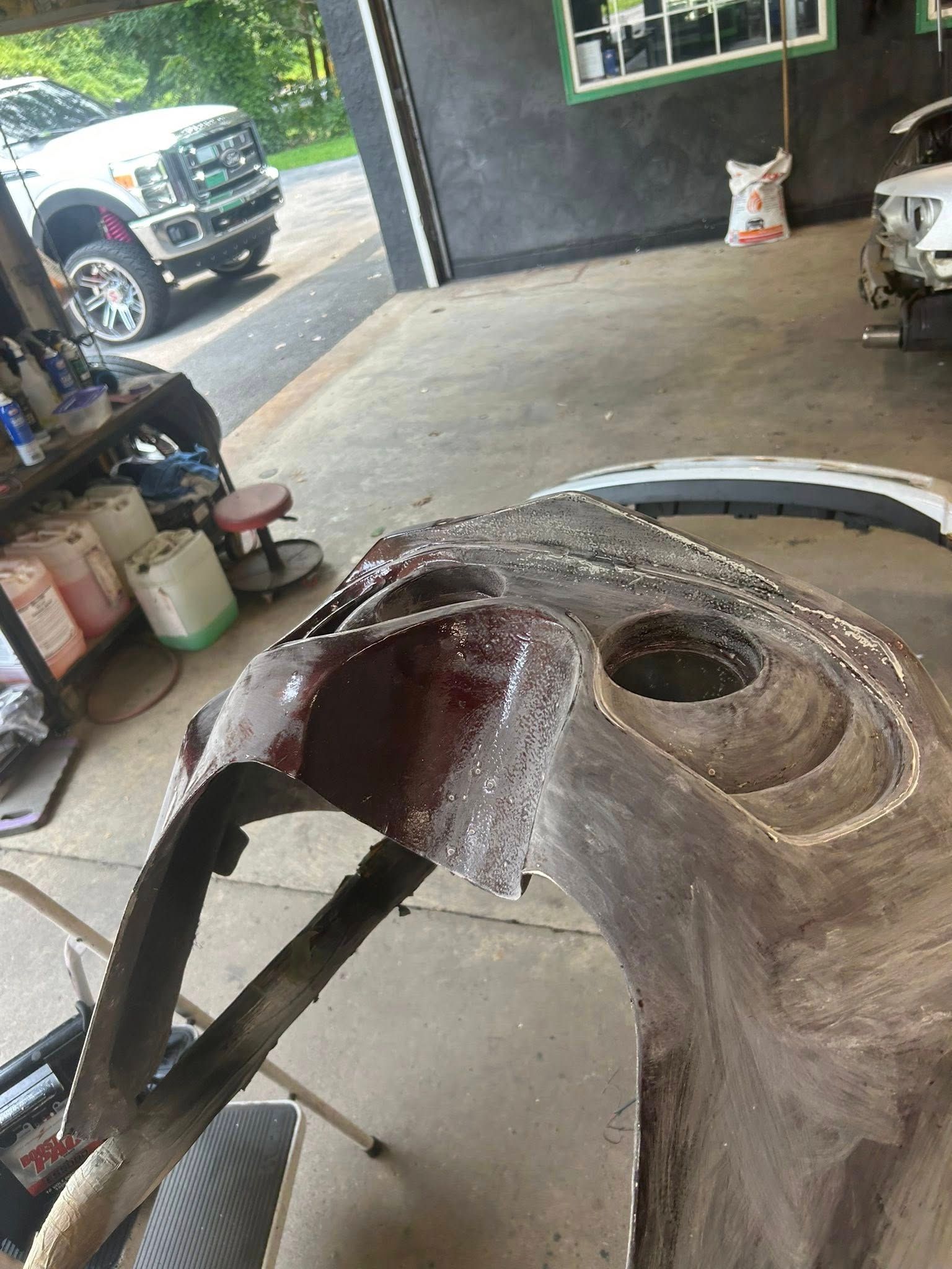 A car bumper being worked on in a garage. Shows the bumper up close with a Ford truck in the background.
