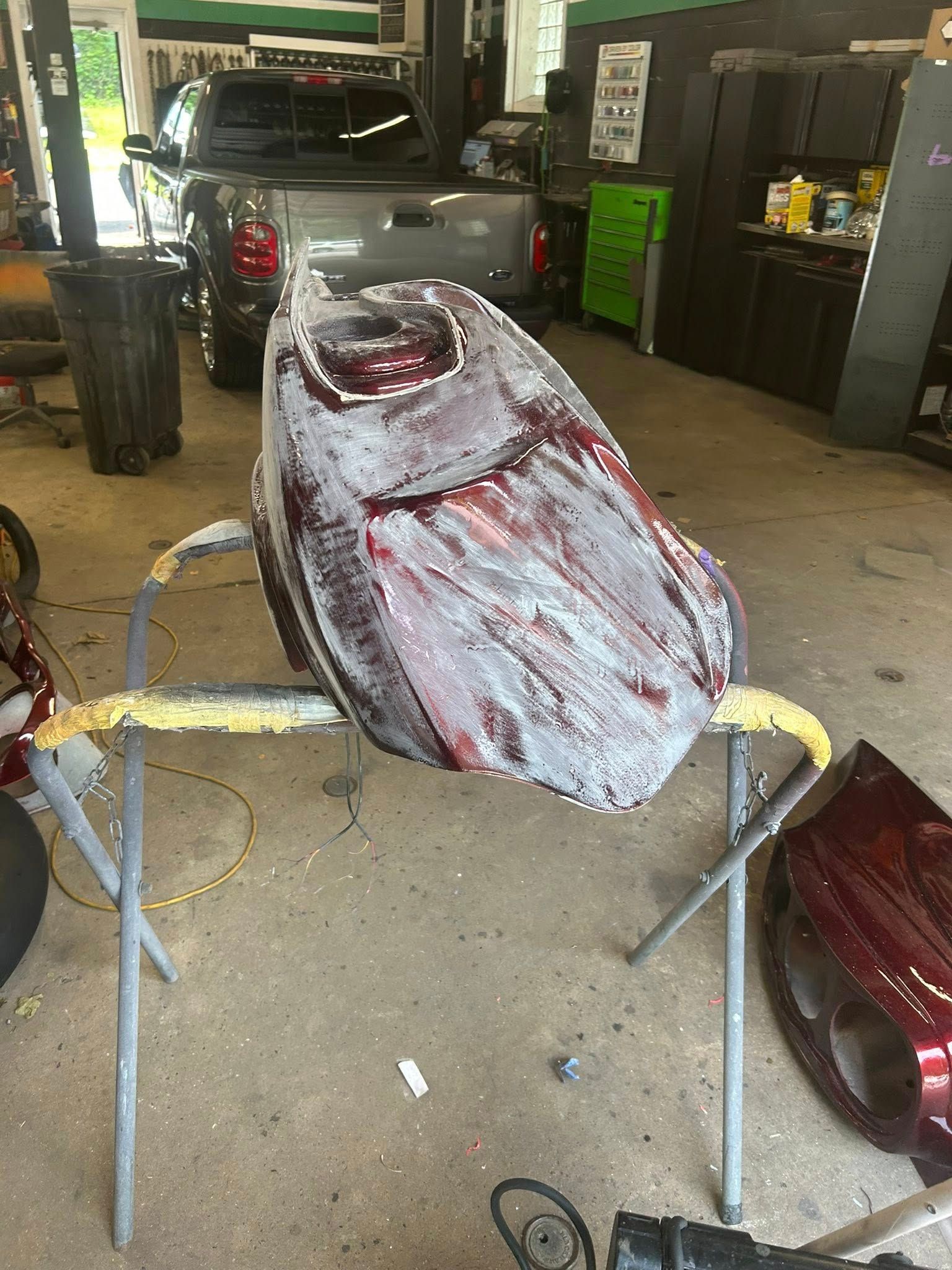 Motorcycle gas tank covered in sanding primer, on a repair stand in a garage.