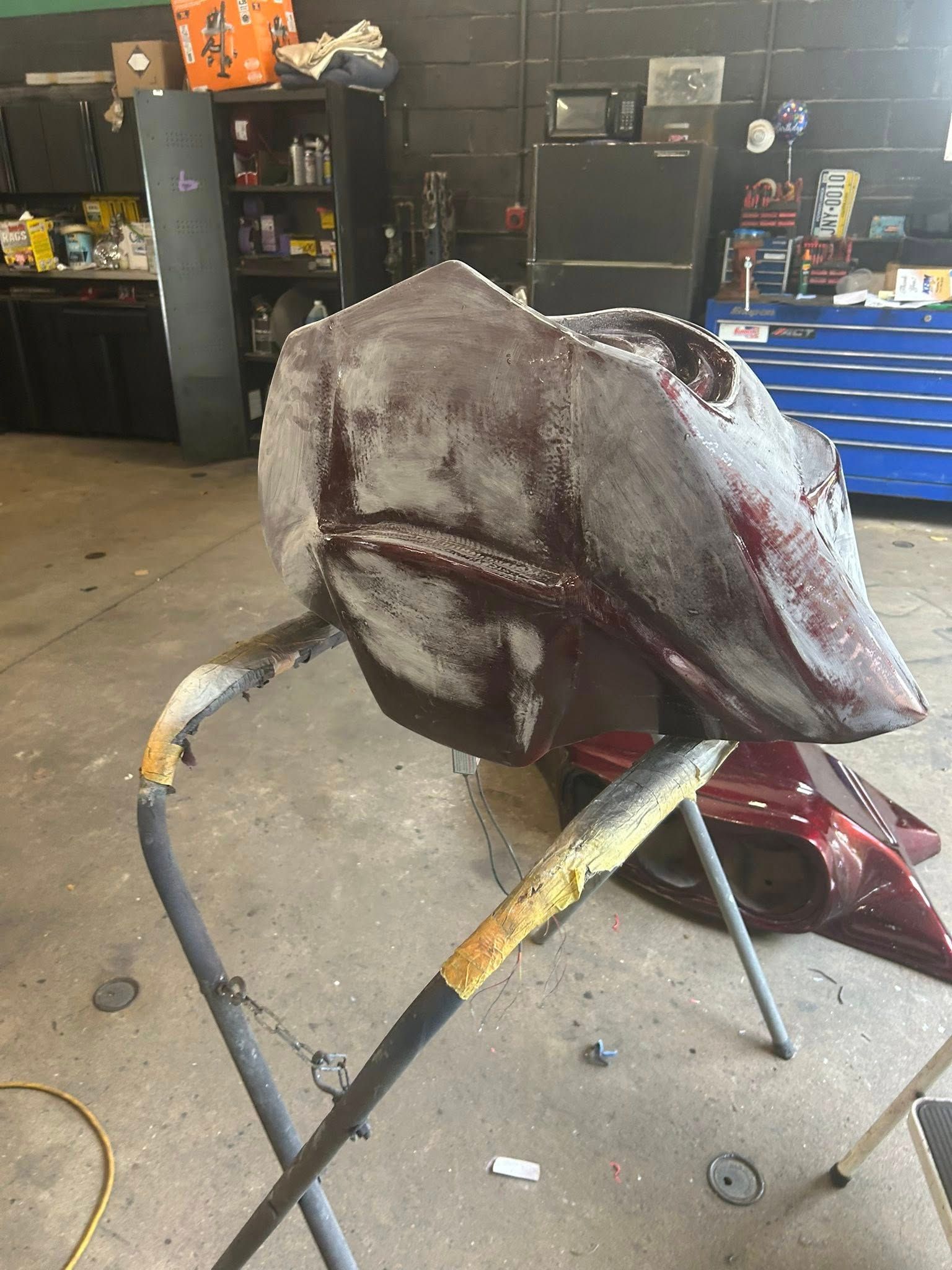 Maroon motorcycle gas tank being worked on in a garage; supported by a stand.