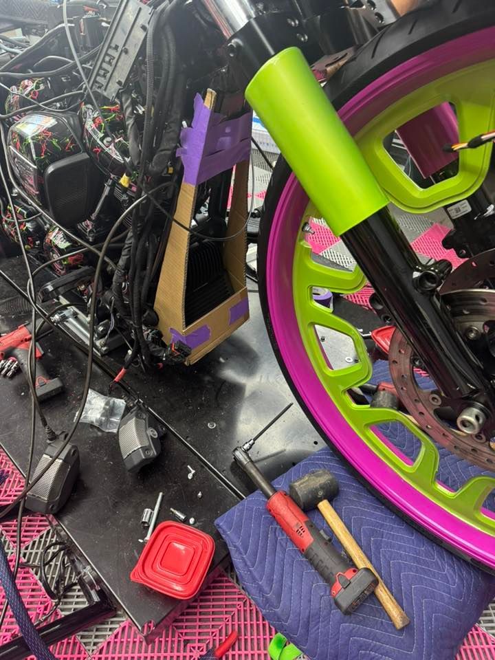 Motorcycle being worked on, with bright pink and neon green accents. Tools and parts are scattered around.