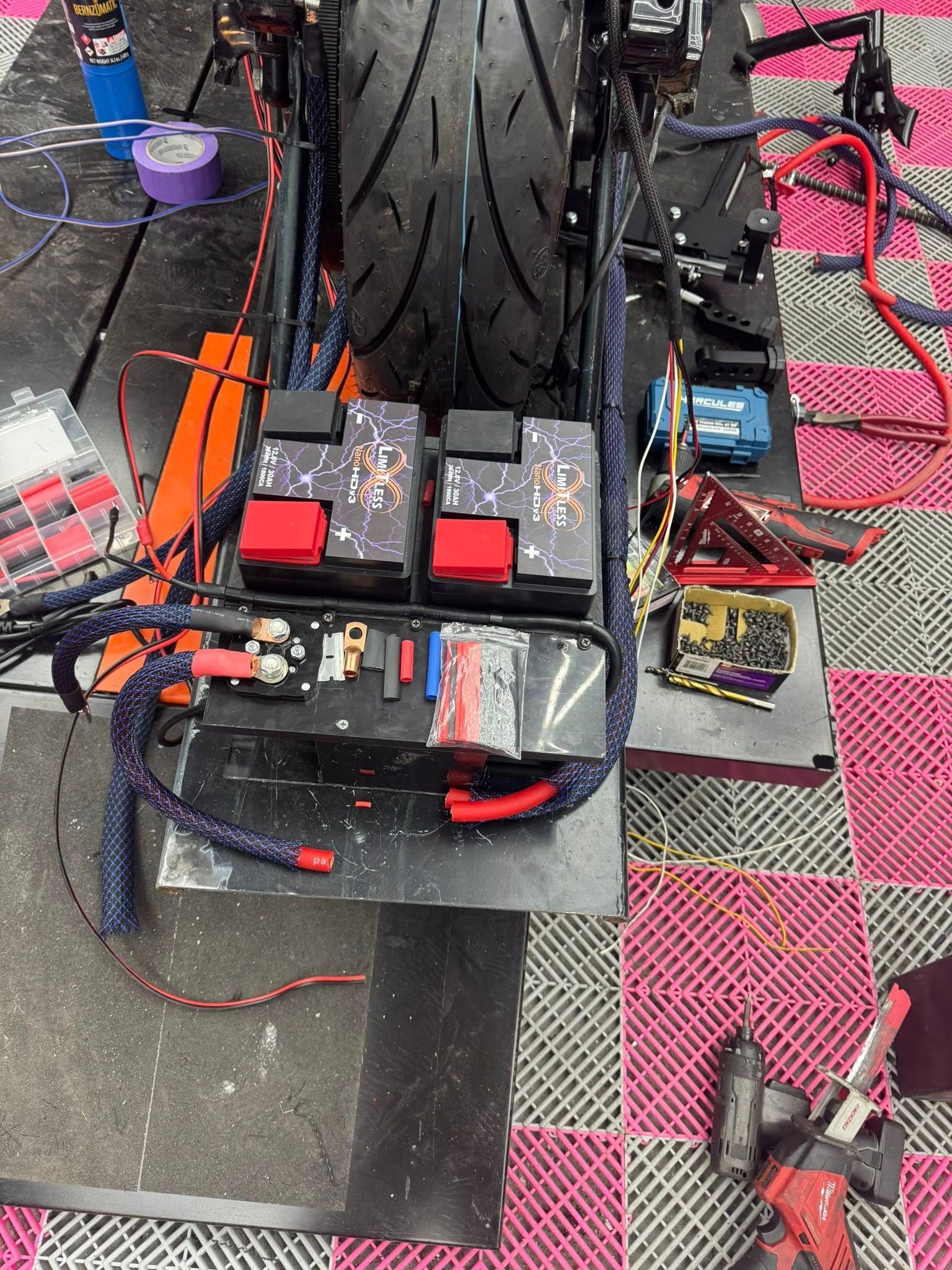 Motorcycle with exposed wiring, tools, and black tire on a pink and black tiled floor.