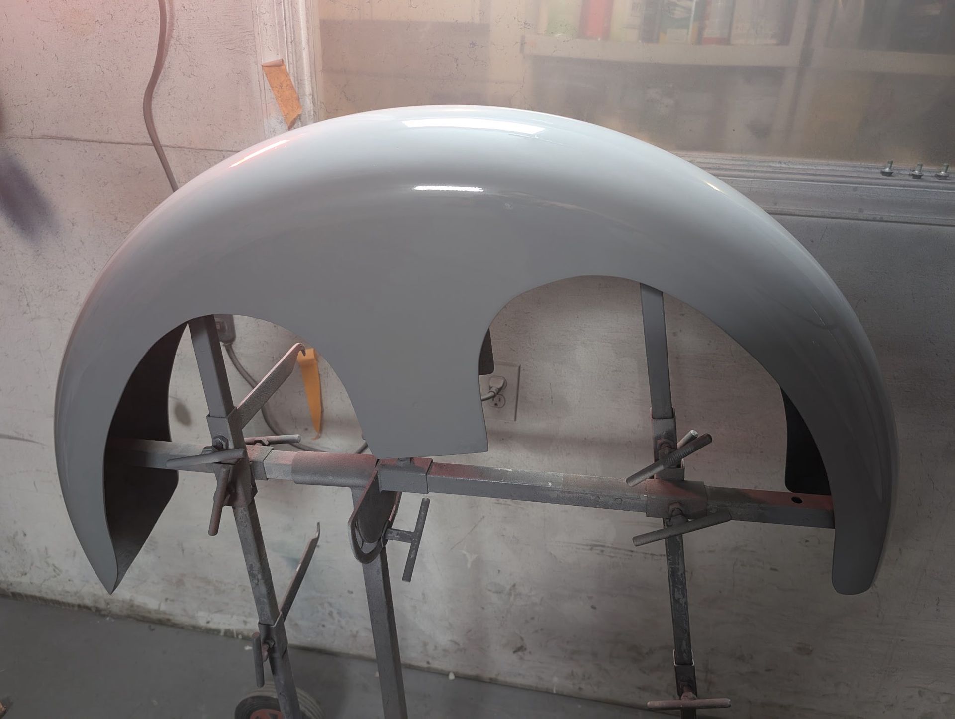 A light gray car fender, freshly painted, mounted on a stand in a workshop.