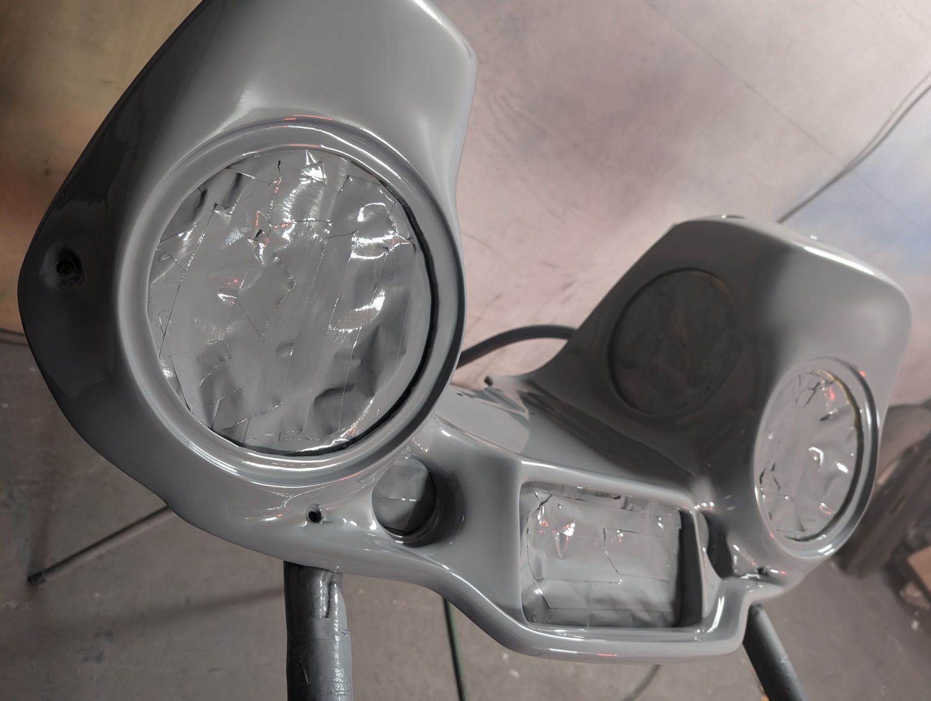 Gray motorcycle fairing with circular headlight and speaker openings, resting on a stand.