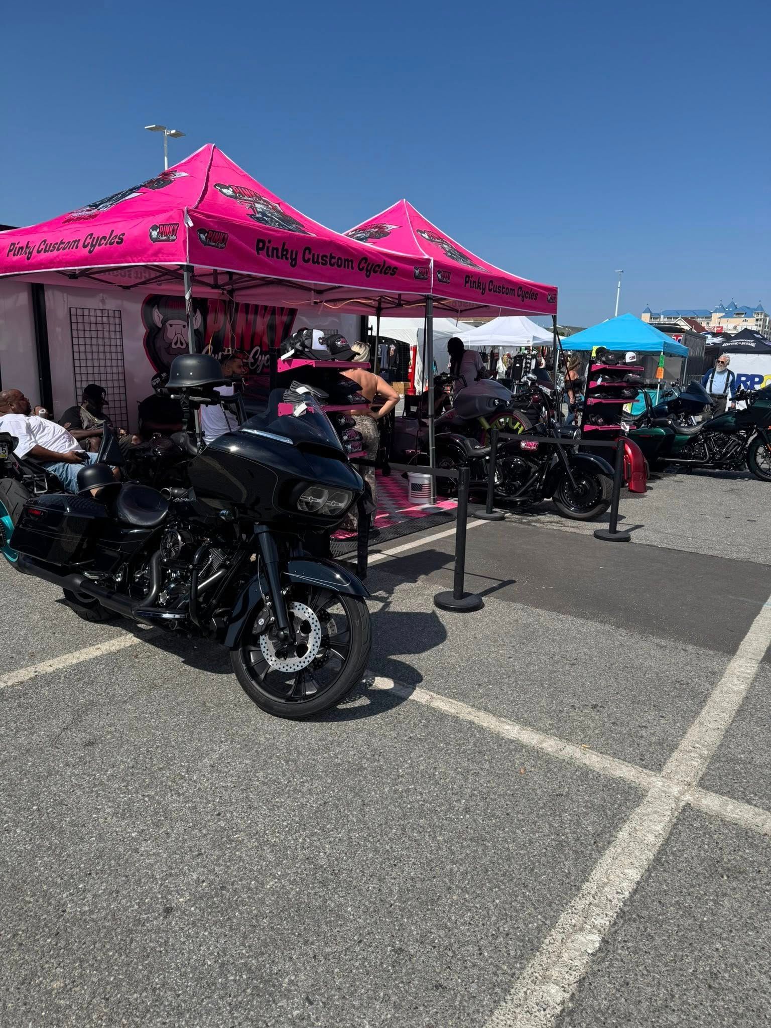 Motorcycle event with black bikes parked near pink vendor tents under a blue sky.